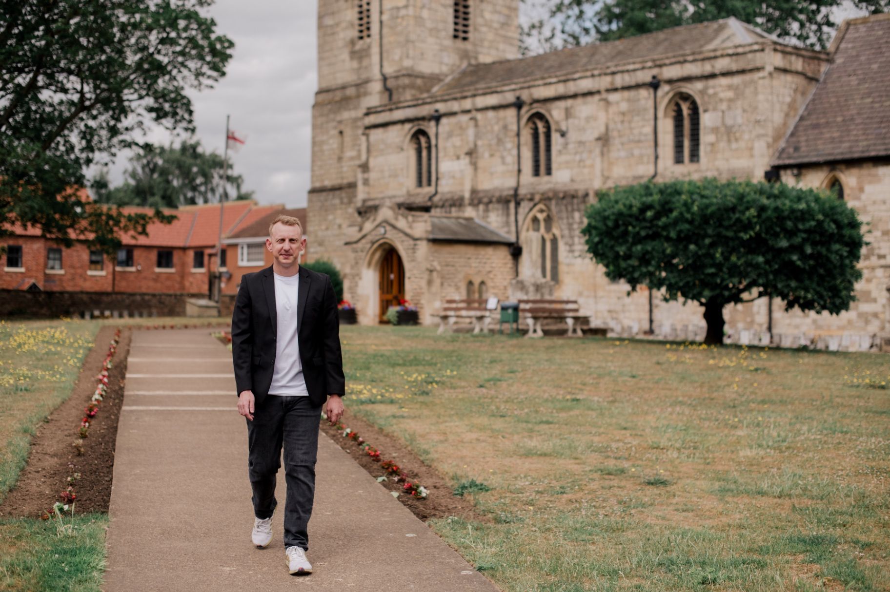 Oliver walking through a garden pathway with a historic church and greenery