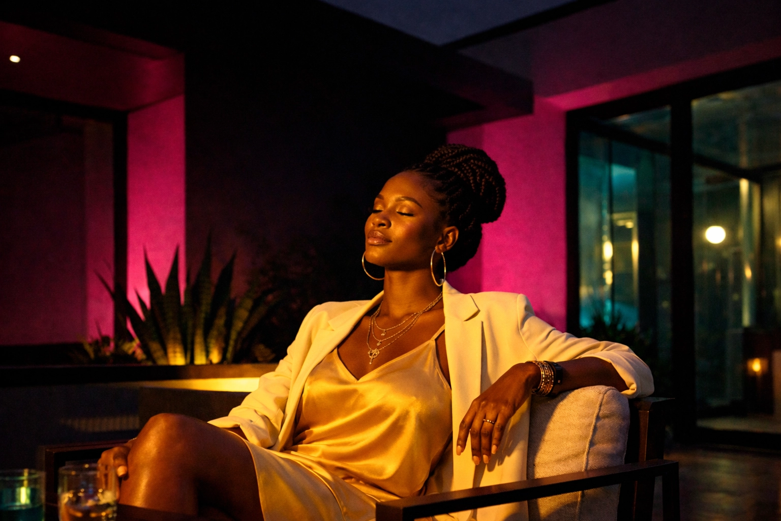 Stylish Black woman relaxing on a chic outdoor patio with warm architectural lighting for a sanctuary vibe.