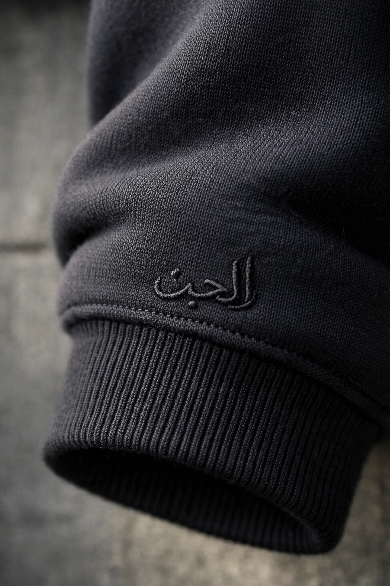 Close-up of subtle Arabic calligraphy on minimalist Islamic streetwear hoodie sleeve for daily Niyah.
