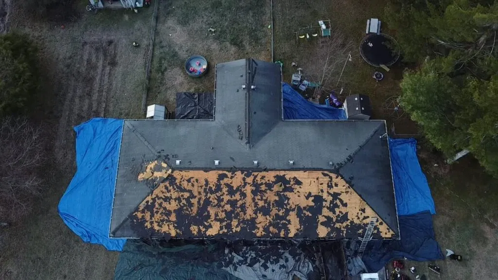 Aerial view of a residential roof replacement showing professional debris management and tarps