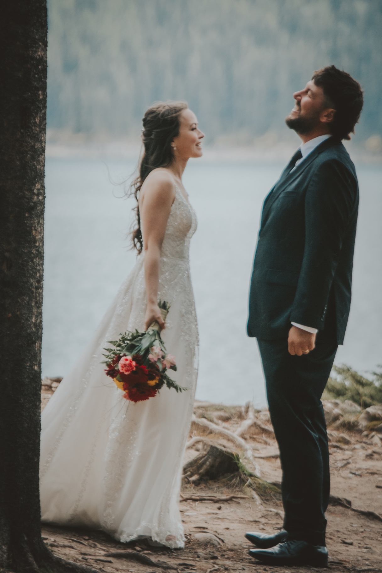 A bride in a white gown holding a bouquet and a groom in a dark suit share a joyful moment