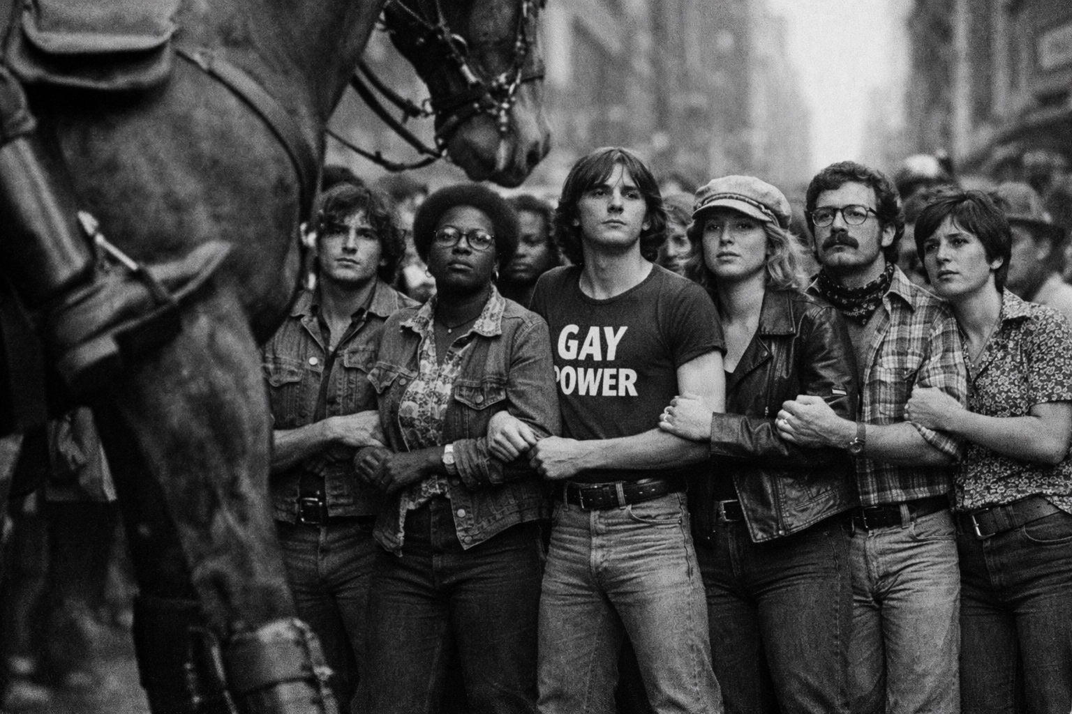 1970s LGBTQ+ activists protesting arm-in-arm against a mounted police horse at an early Pride march.