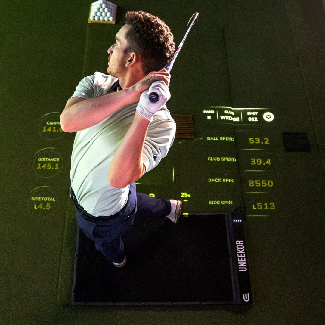 Golfer finishing a swing on a Uneekor hitting mat with real-time data projected onto the floor.