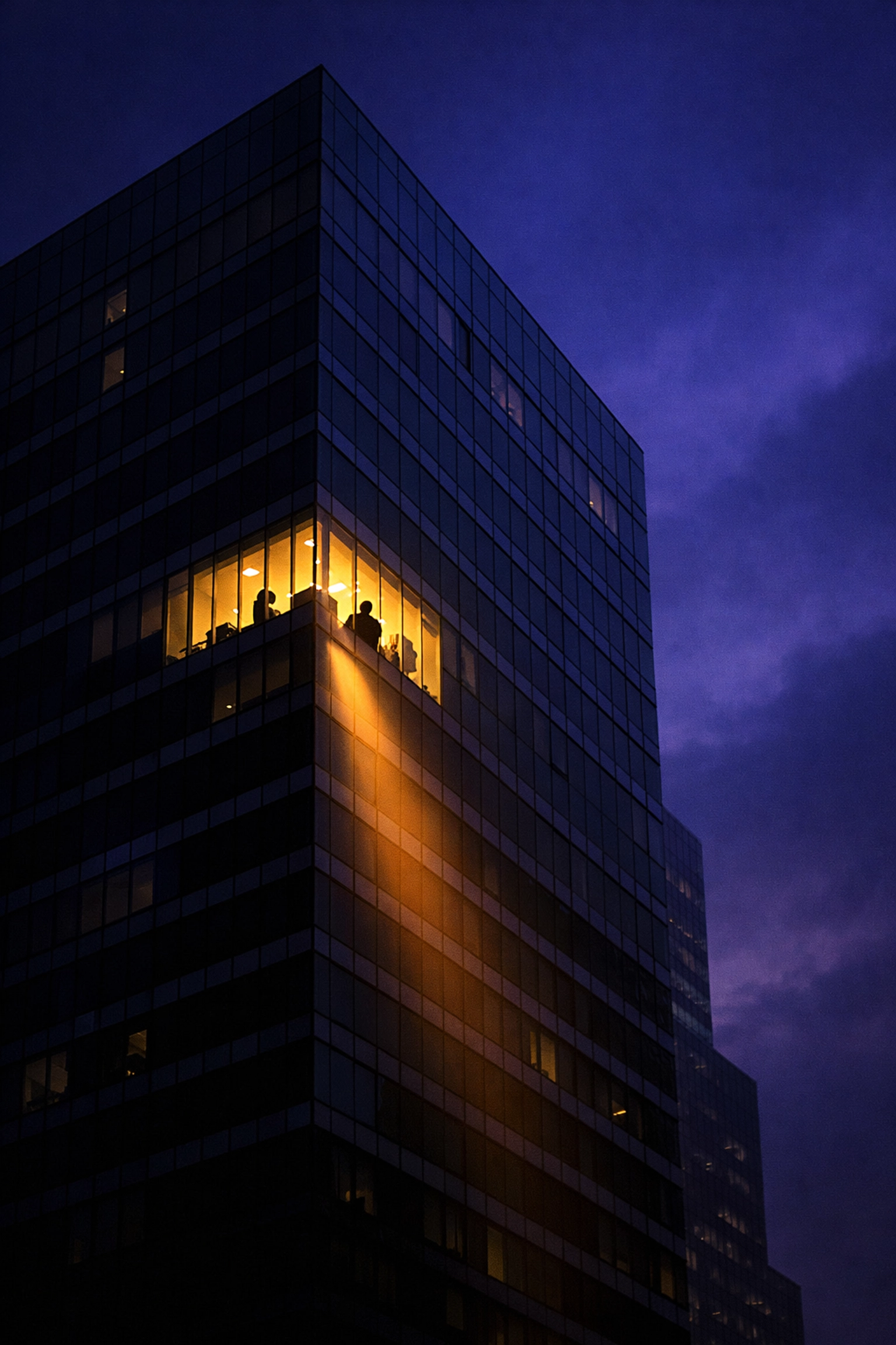 Lone worker in a lighted office window at night symbolizing small business overtime compliance.