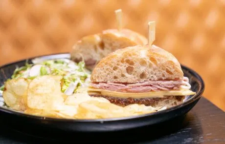 A plate featuring a gourmet sandwich made with rustic bread, ham, cheese, and fresh salad, served in The Colony Group's onsite bar.