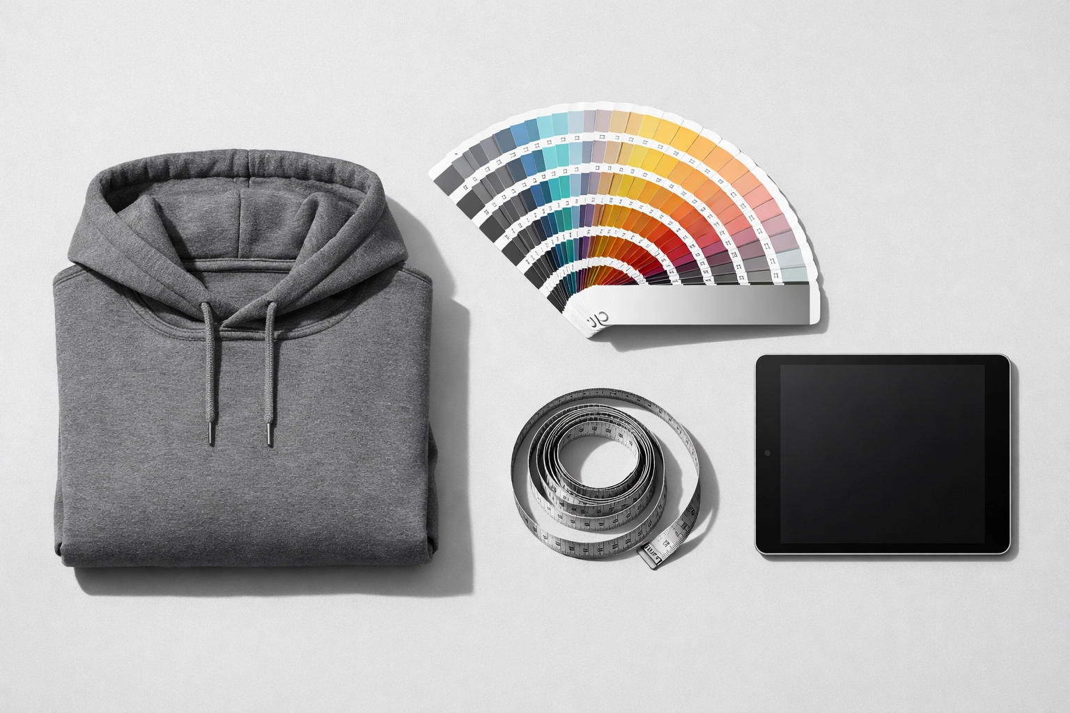 Professional custom apparel planning tools including a folded hoodie, Pantone guide, and measuring tape.