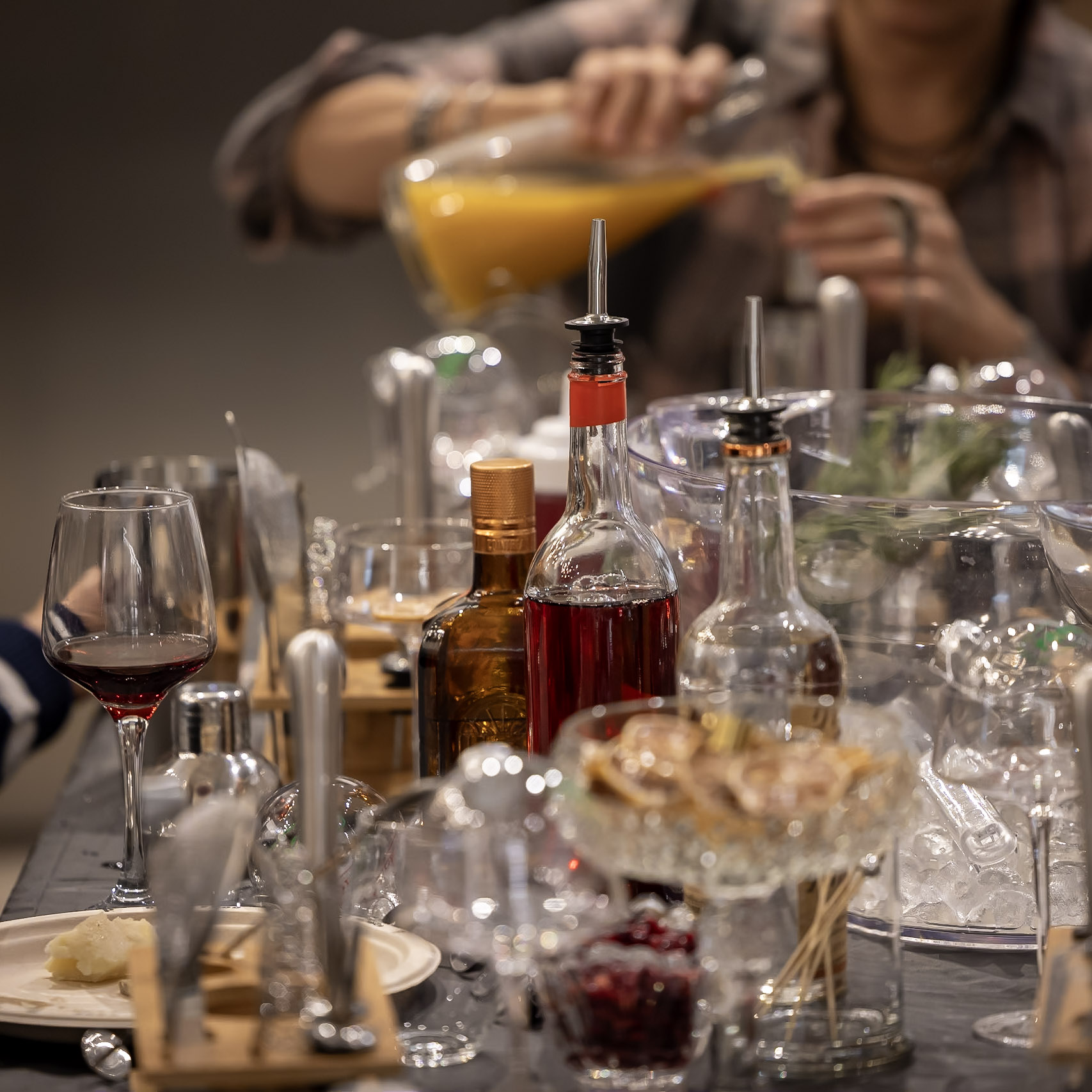 Bar setup featuring assorted spirits, wine, garnishes, glassware, bar tools, and a mixing vessel