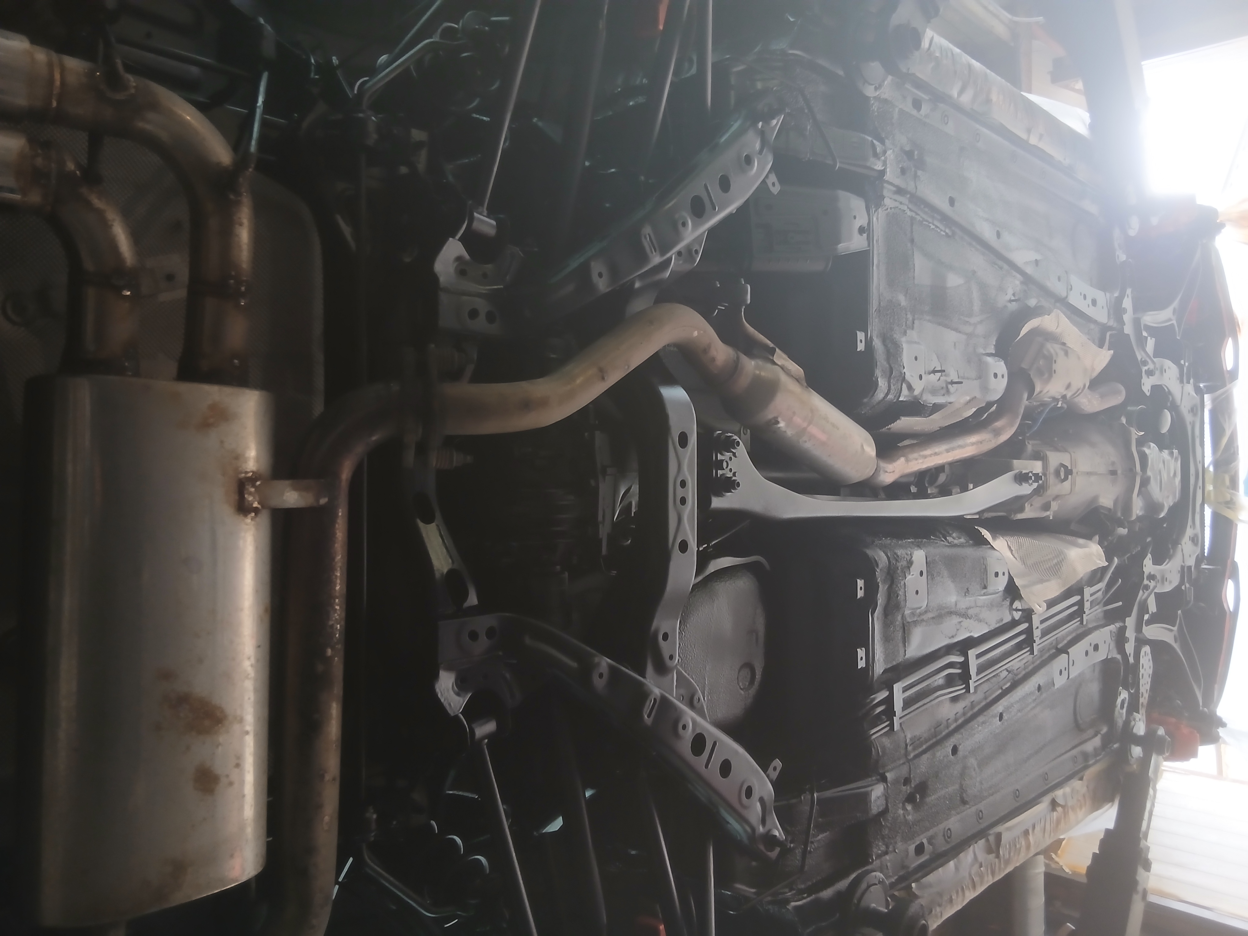 Vehicle underbody view showing the exhaust system, lower chassis, and metal components with visible surface rust.