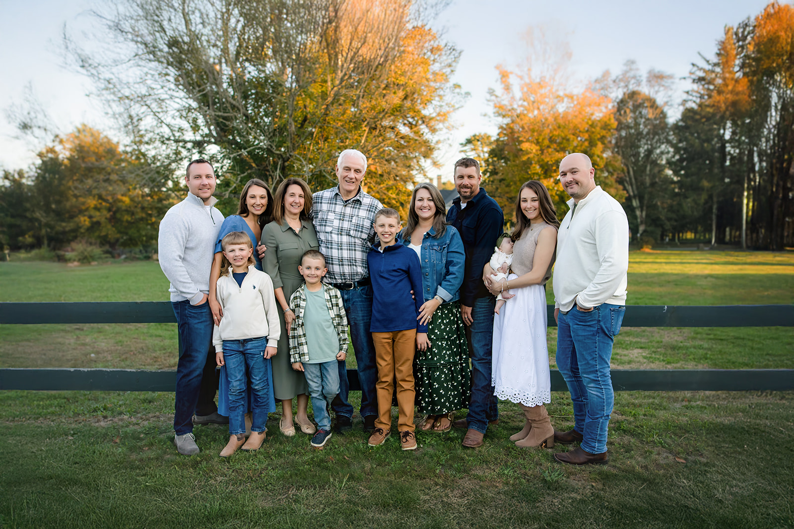 Three generations of a family pose together outdoors, framed by Cape Cod greenery and golden-hour sunlight.
