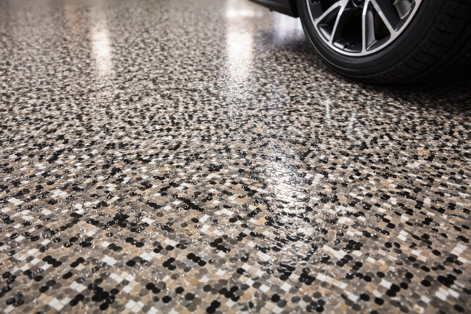 Close-up of a finished polyaspartic garage floor with decorative flakes and a car tire highlighting durability