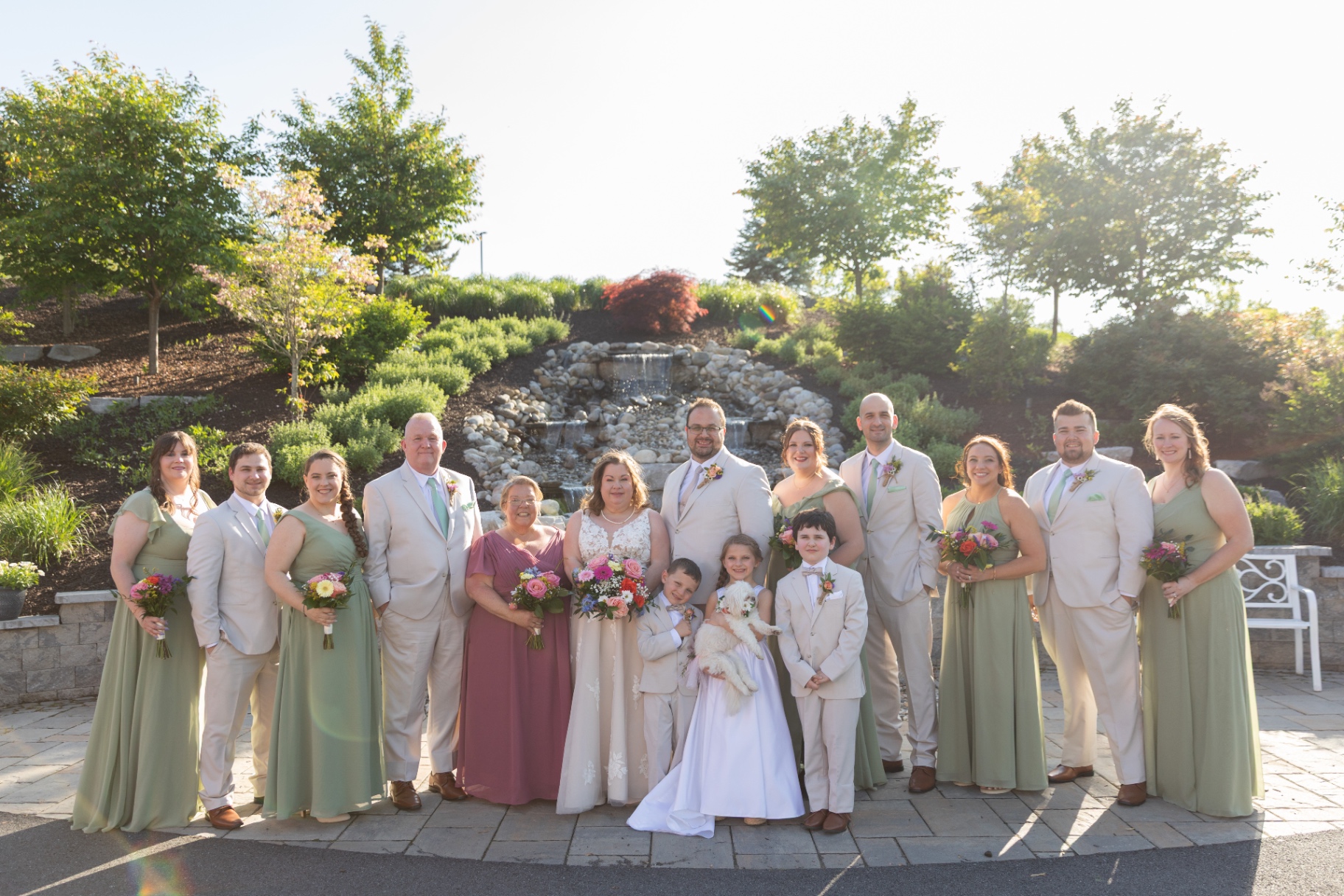 Full wedding party outdoors—classic group portrait with the waterfall behind them