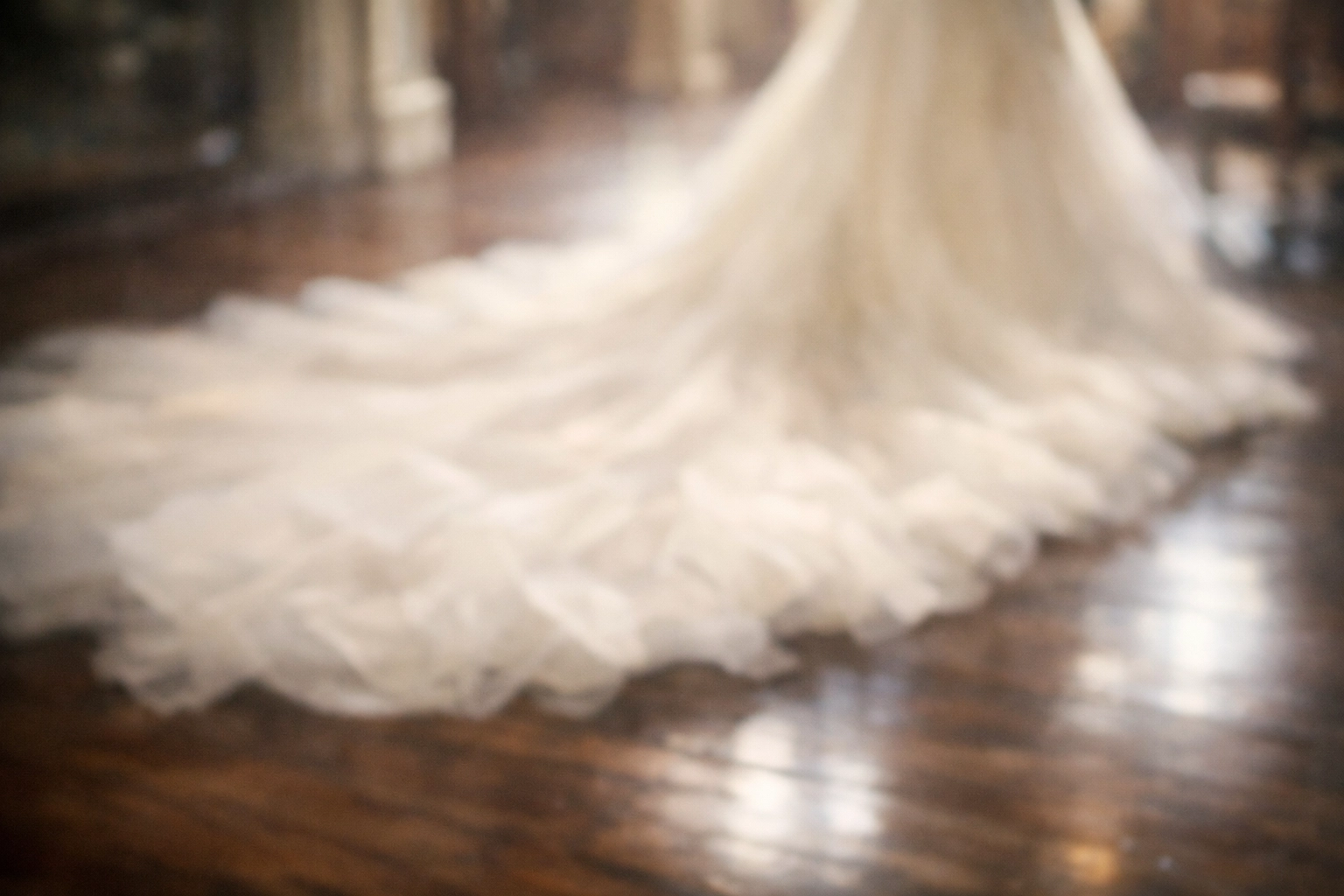 Mysterious out-of-focus view of a voluminous Ariamo couture wedding dress train pooling on a wood floor.
