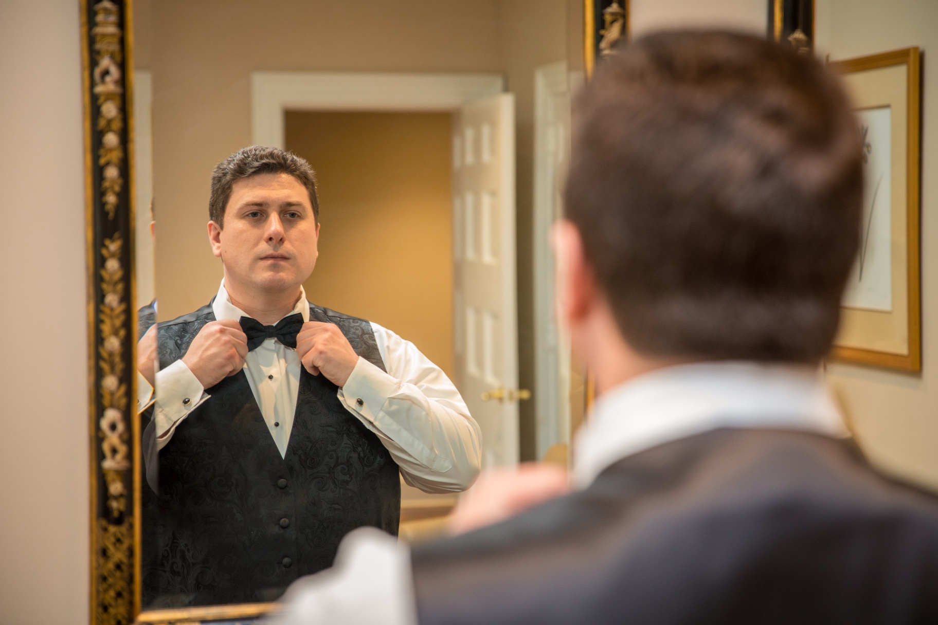 Groom standing by a softly lit window in a white tuxedo jacket