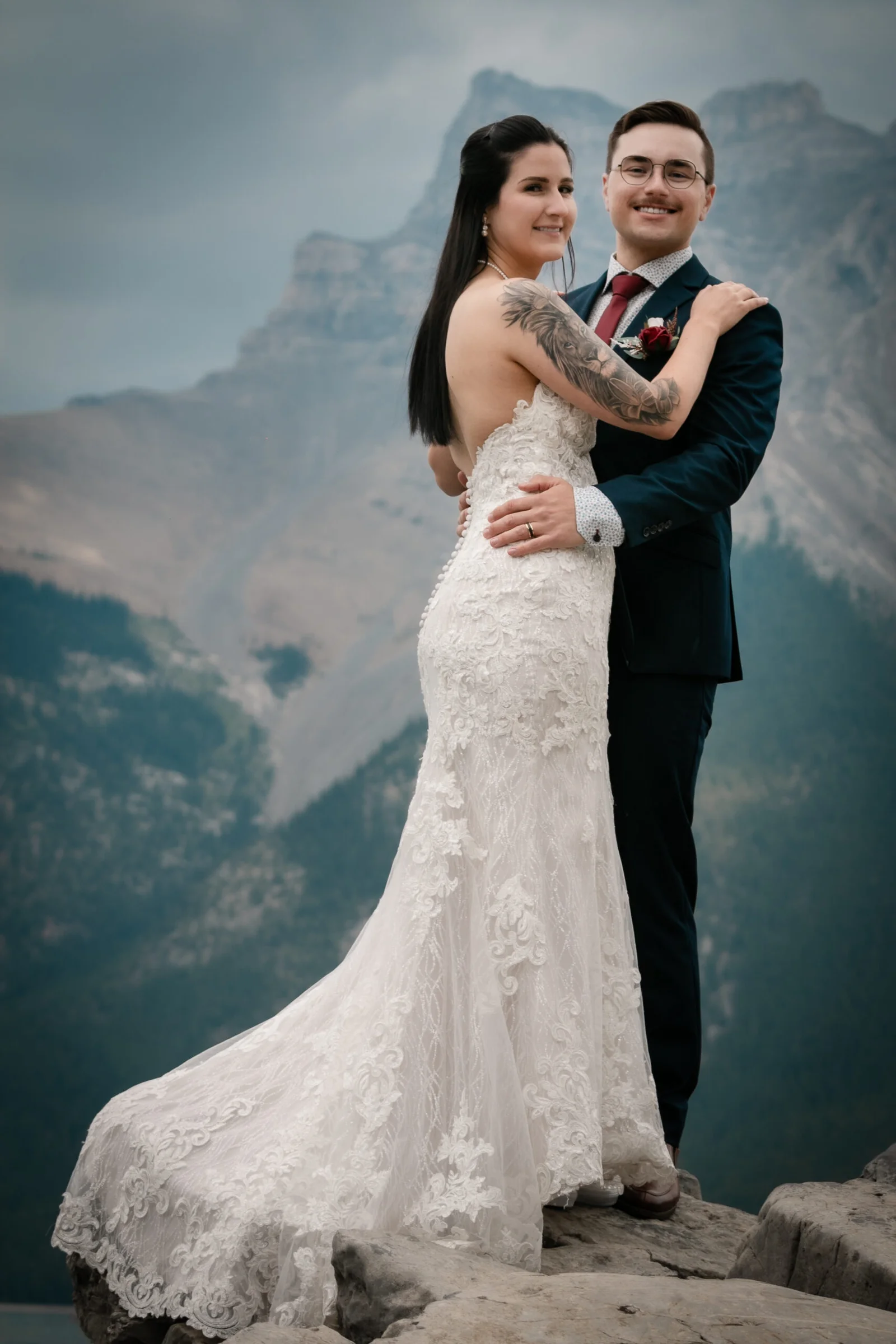 A couple stands on rocky terrain in wedding attire