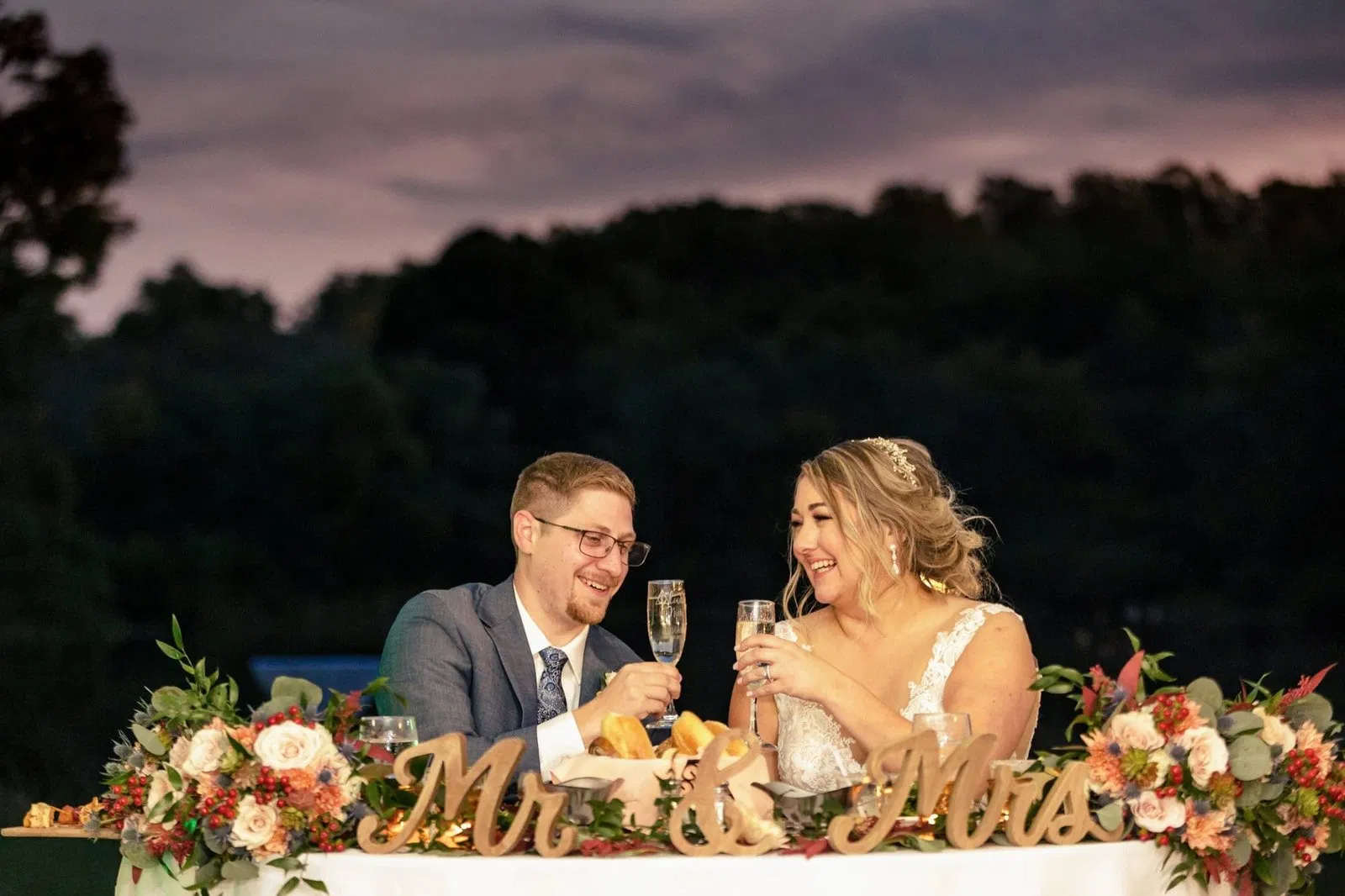 Intimate close-up of a bride and groom toasting with champagne flutes at a floral-decorated sweetheart table