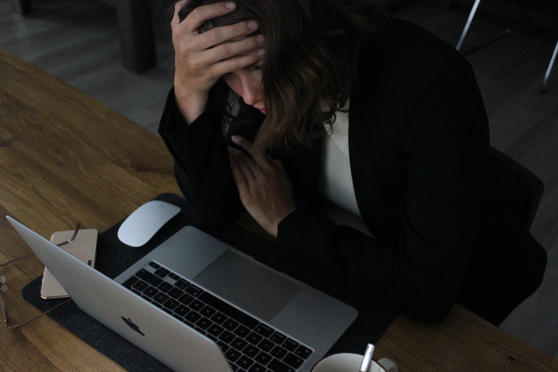 [Workplace Burnout (Before Intervention) An employee in business attire sits at a desk with a laptop, head in hand, visibly stressed or overwhelmed. Surrounding items include a smartphone, glasses, and a cup, suggesting a typical work environment. This image reflects workplace burnout before intervention.]