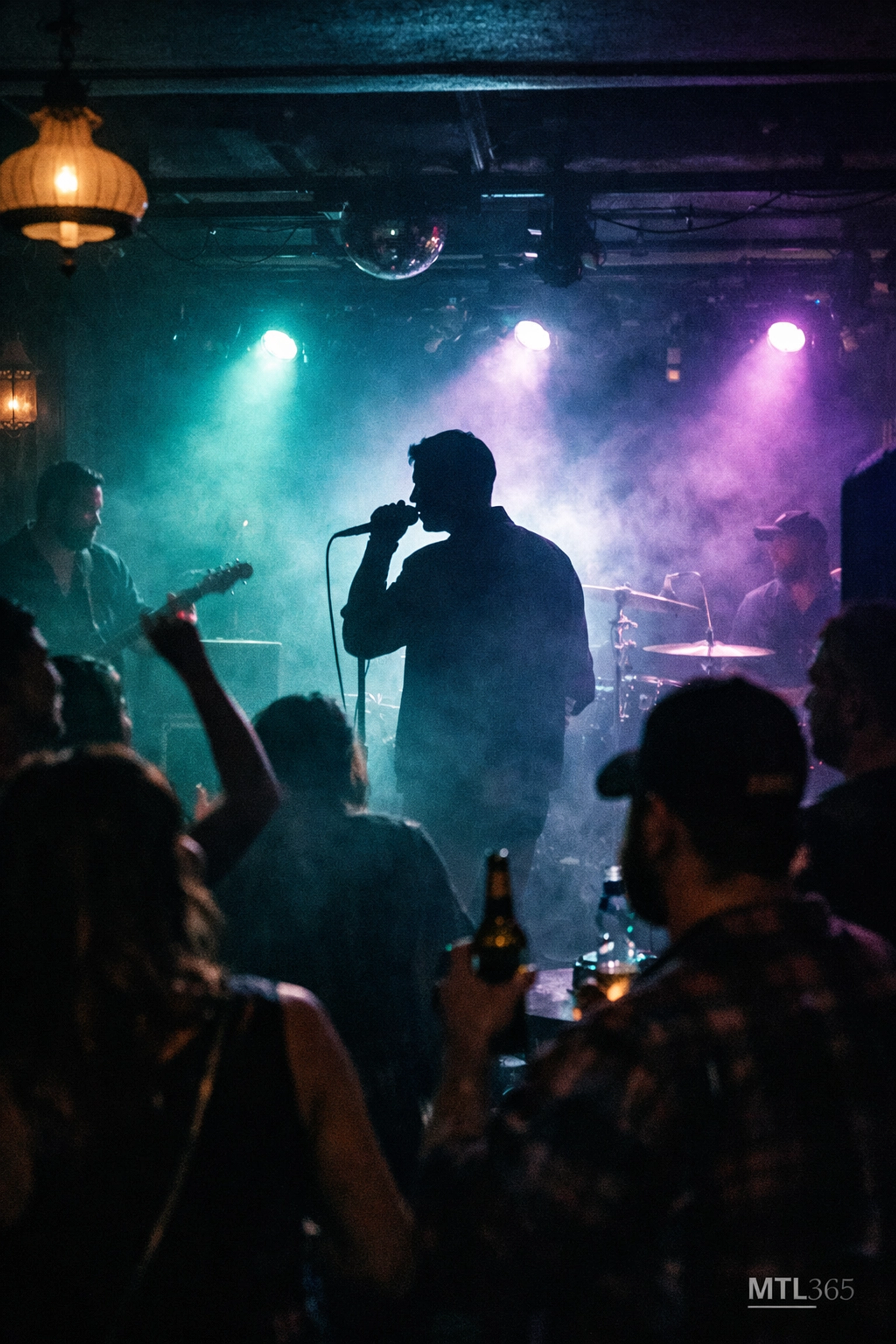 Crowded Montreal live music club with a band performing under vibrant teal and violet stage lights.