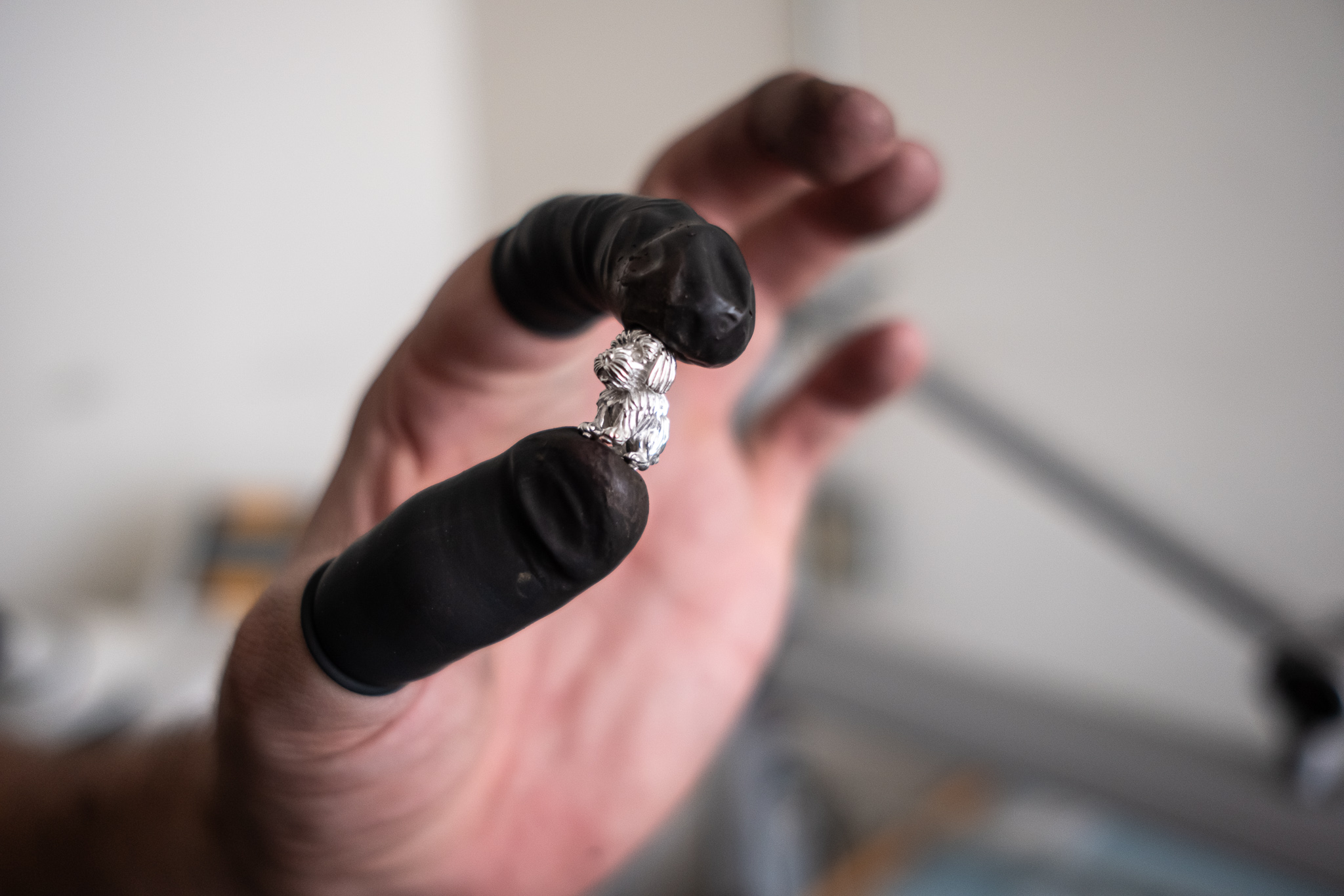 A jeweler’s gloved hand holds a freshly cast, unpolished metal charm