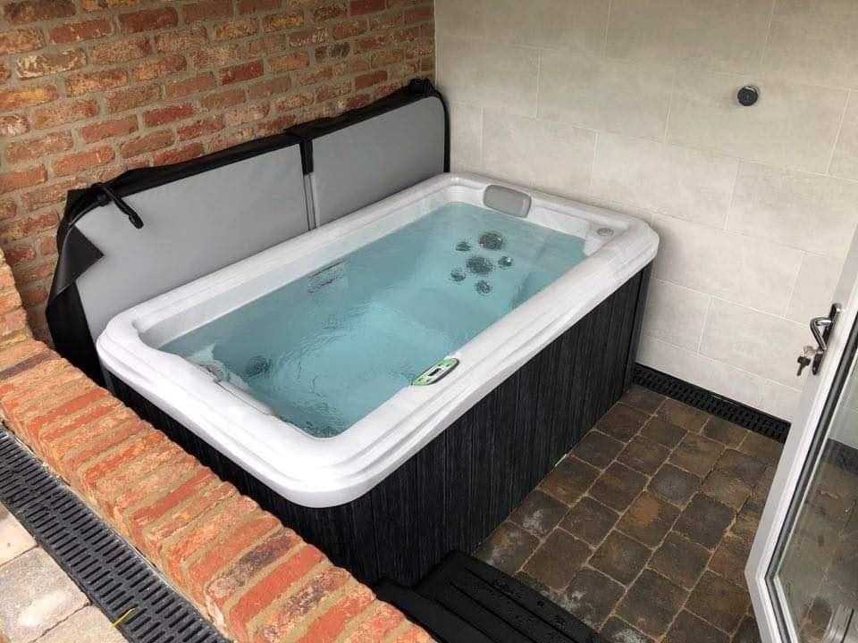 Compact premium Artesian Spa hot tub installed in a covered, brick-walled patio area