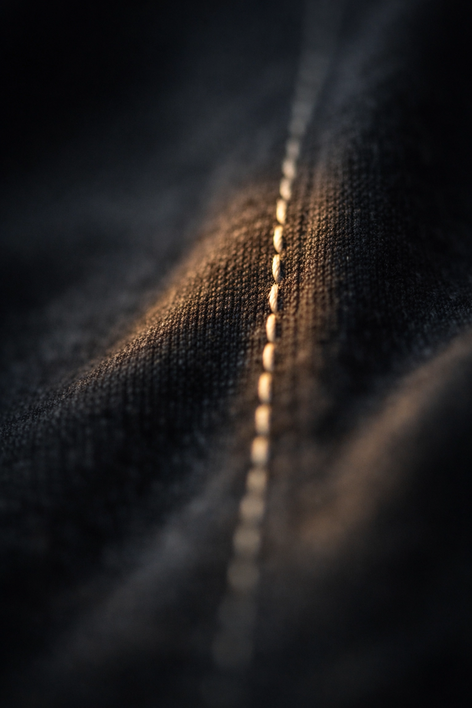 Close-up of charcoal fabric and stitching in soft light, representing resilience and identity in mental health recovery.