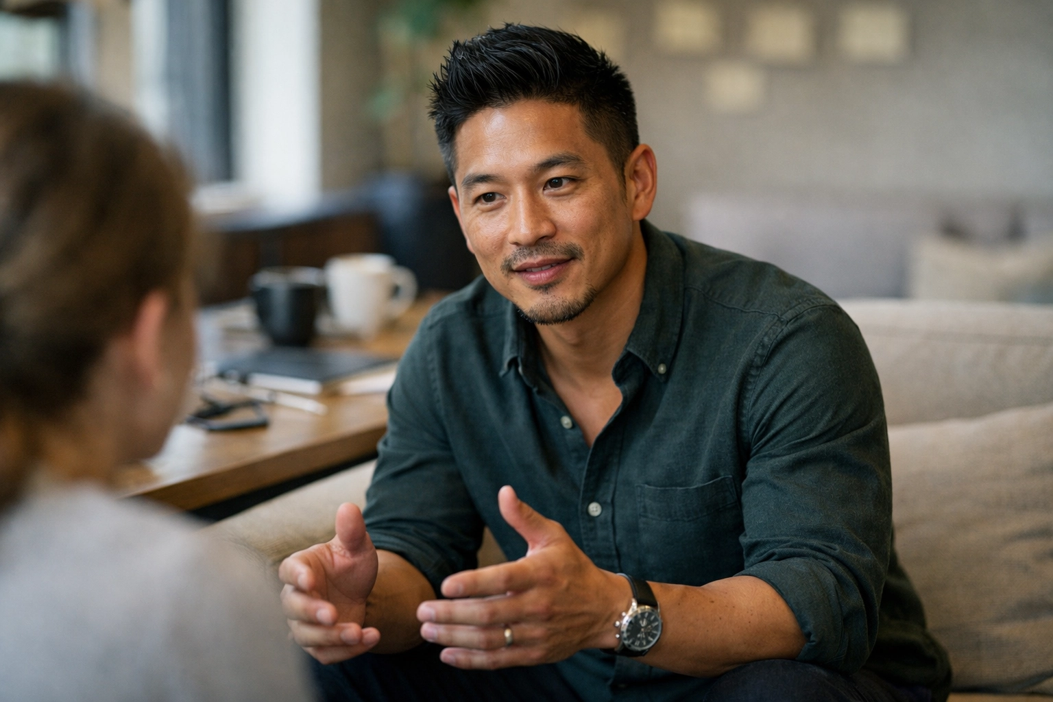 One-on-one coaching conversation with Jordan Lee—cinematic natural lighting, shallow depth of field, and a real desk mess (mugs, cables, notes).
