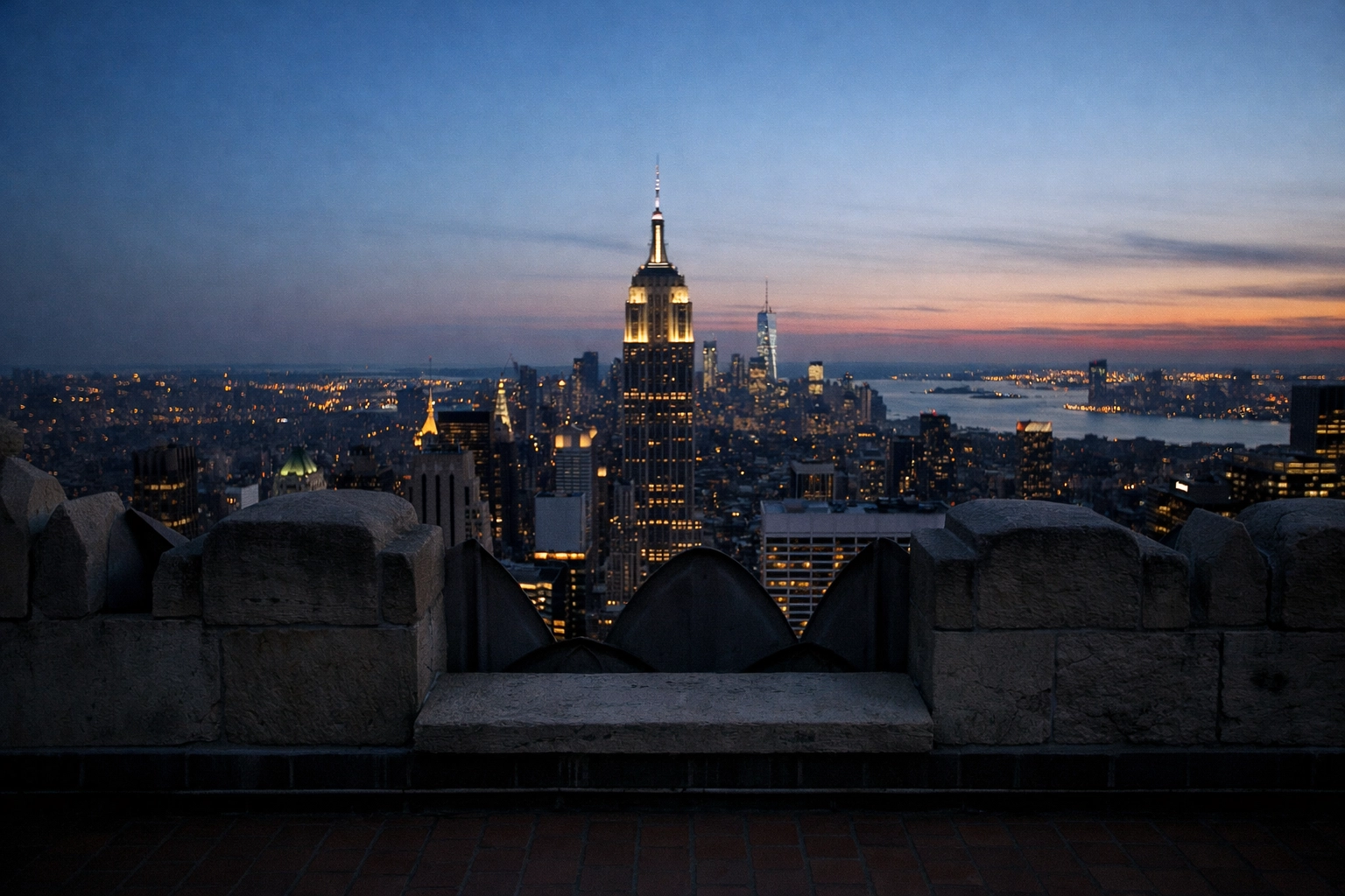 Open-air view of the Empire State Building and NYC cityscape at twilight from Top of the Rock observation deck.