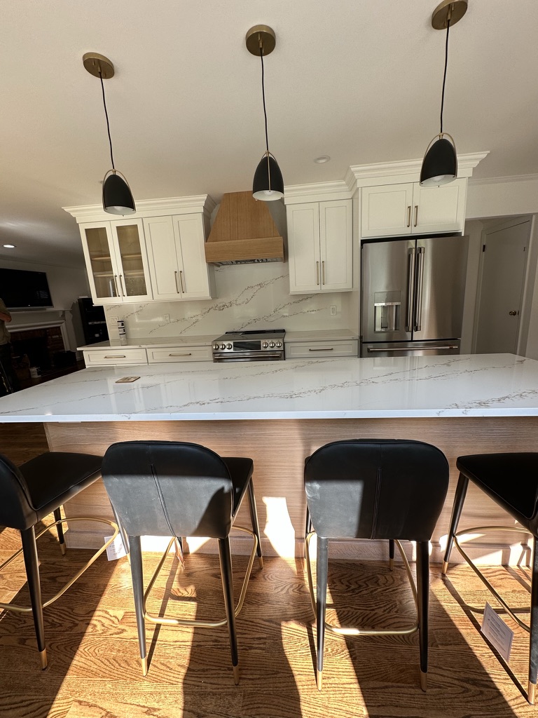 A professionally designed custom kitchen featuring a large island with waterfall marble countertop, integrated wood paneling, and contemporary black/gold bar stools.