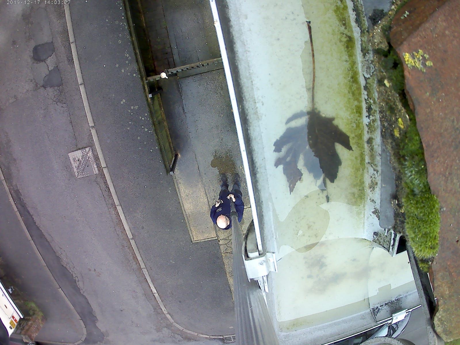 A top-down view showing a technician using a vacuum extension from the ground to clear a residential gutter.