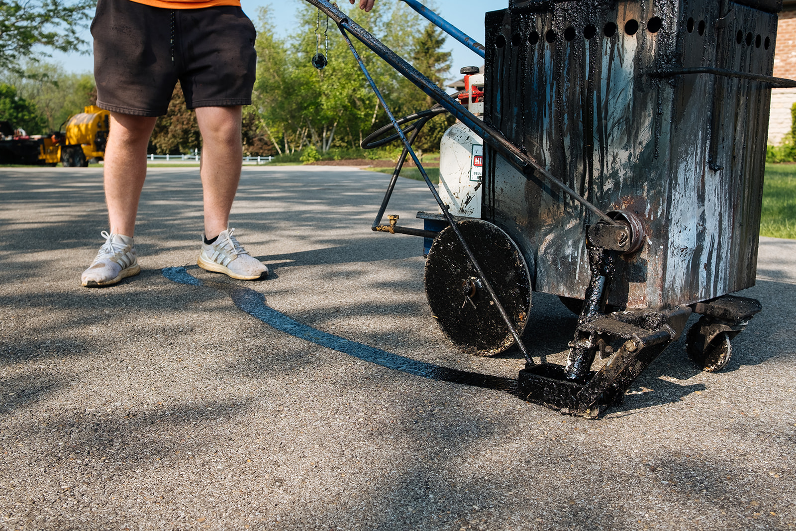 A worker uses a professional crack-sealing machine to apply hot rubberized sealant to asphalt pavement