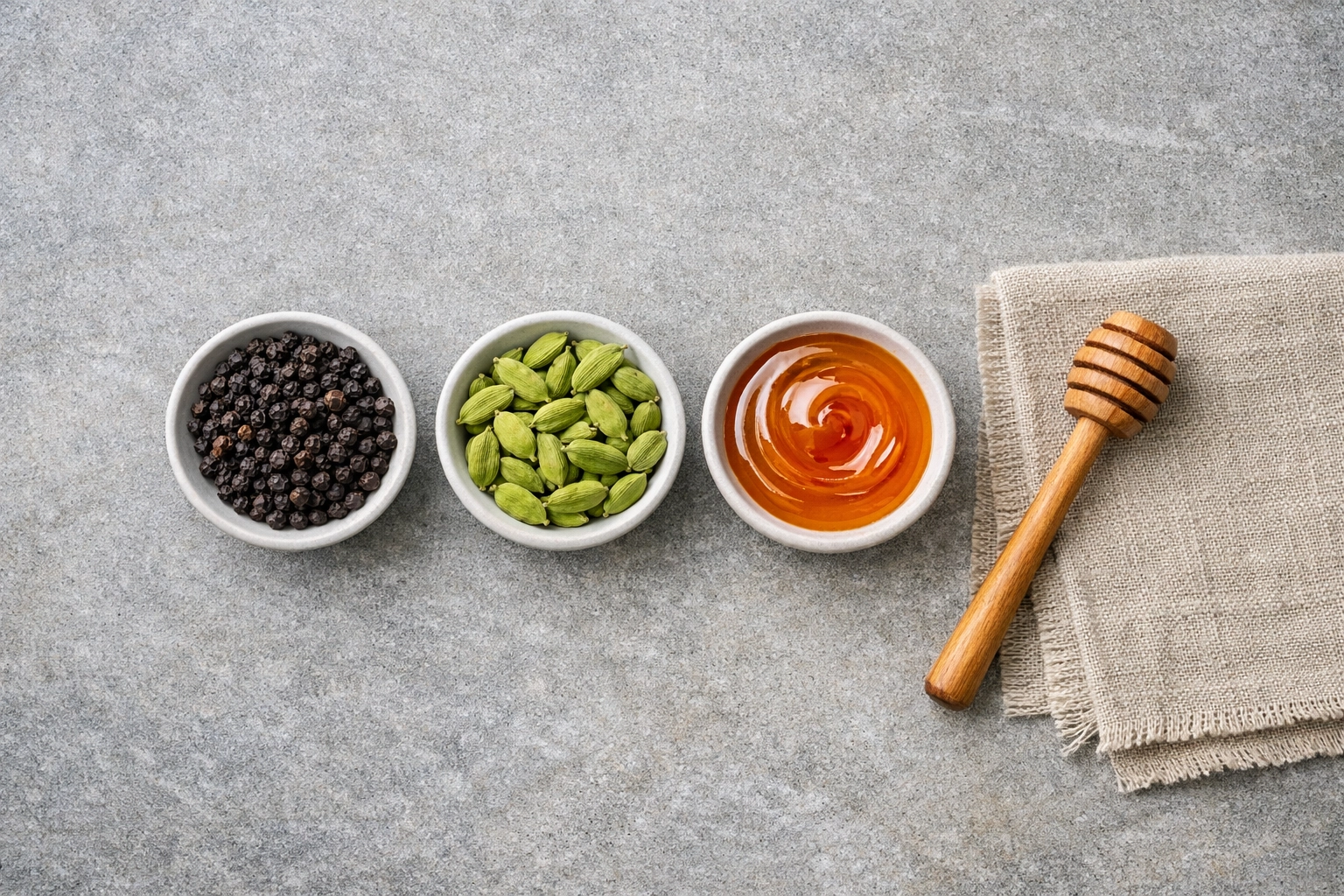 Premium Tellicherry black pepper, cardamom, and organic honey in ceramic bowls for a spice gift box.