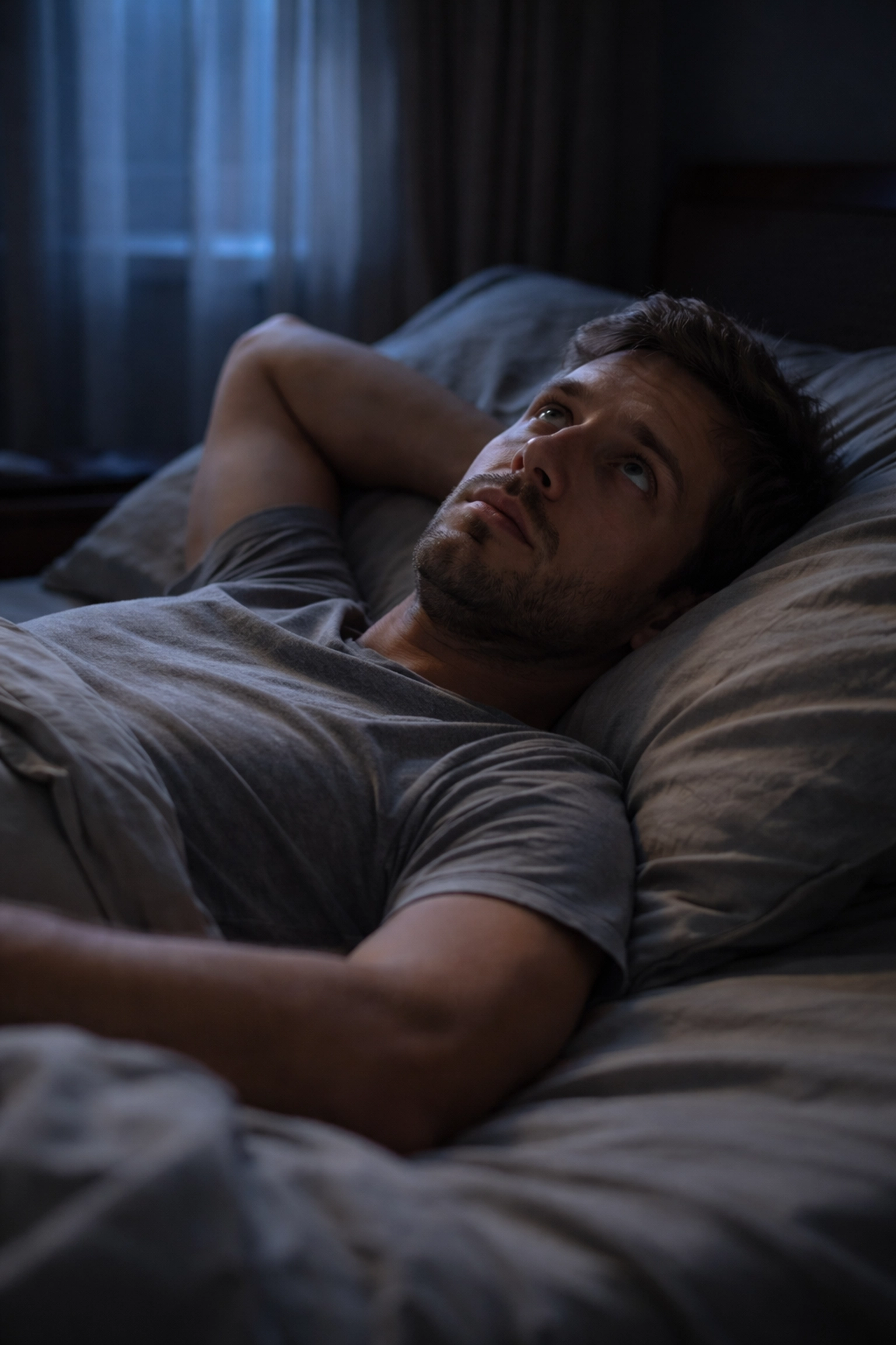 Fáradt férfi álmatlanul fekszik az ágyban, merevedési zavar stressz és alvásproblémák miatt.