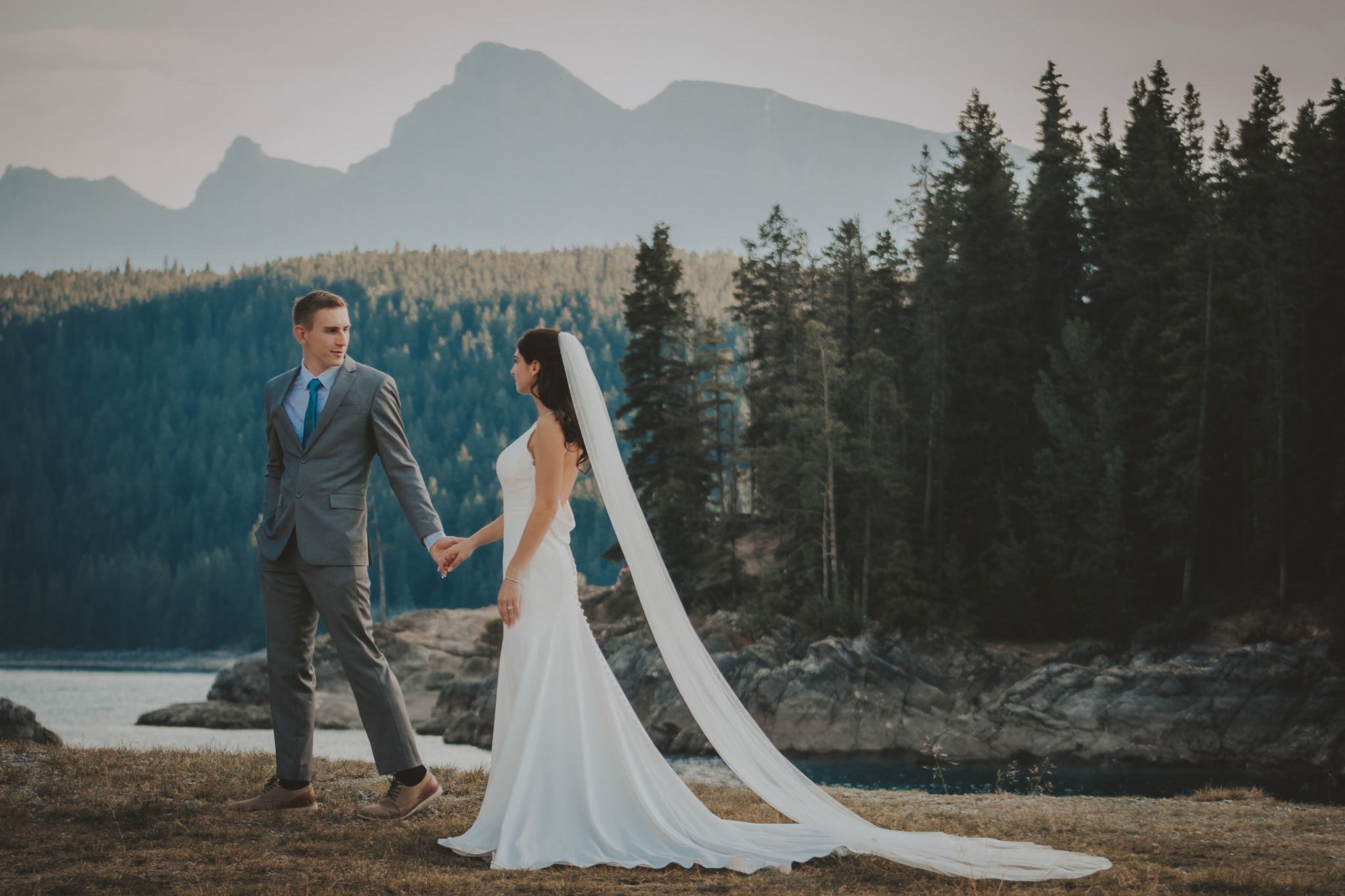 Bride and groom hold hands beside a turquoise lake