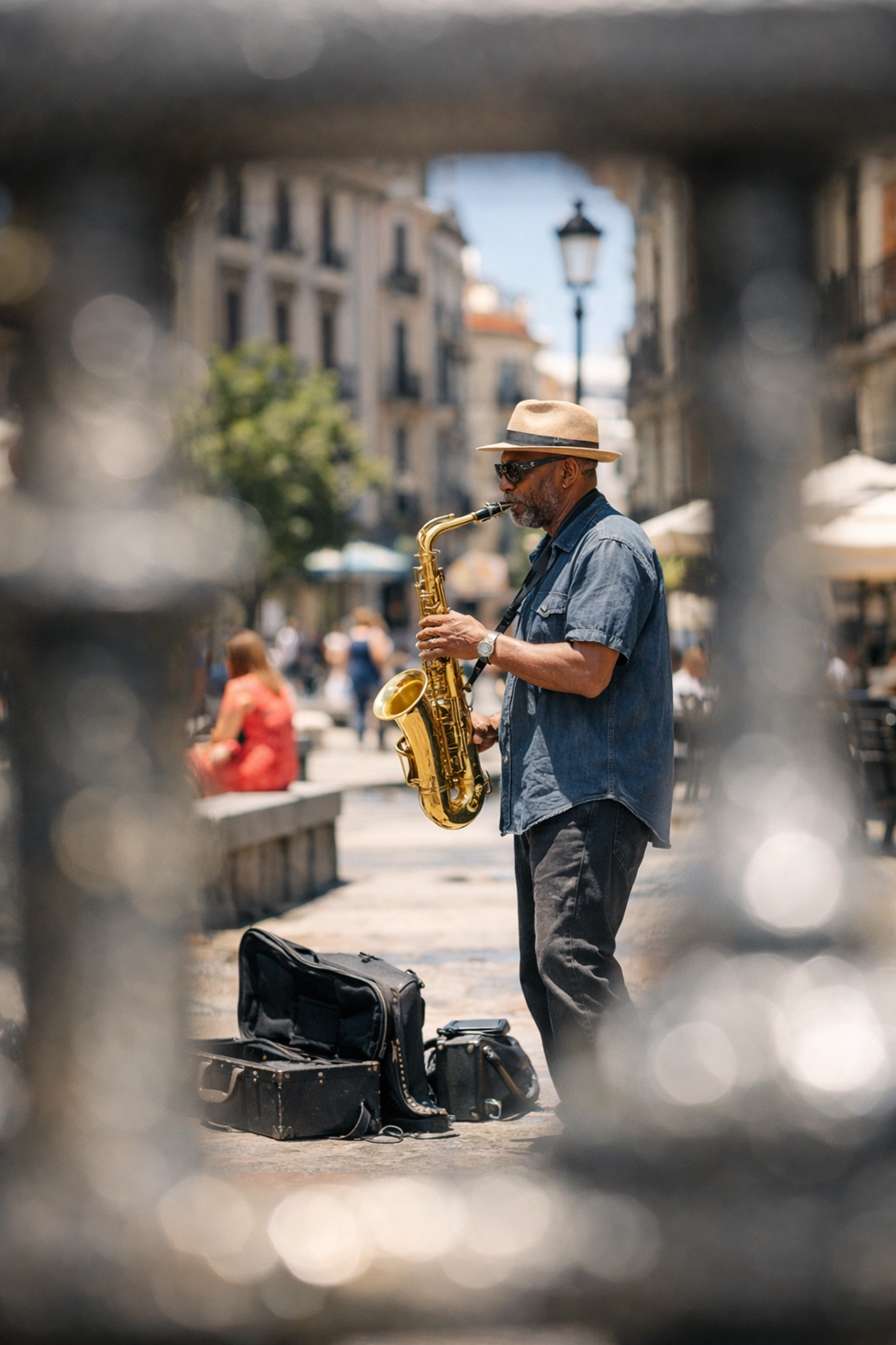 Street photography foreground framing using bridge railings to capture a distant street performer.