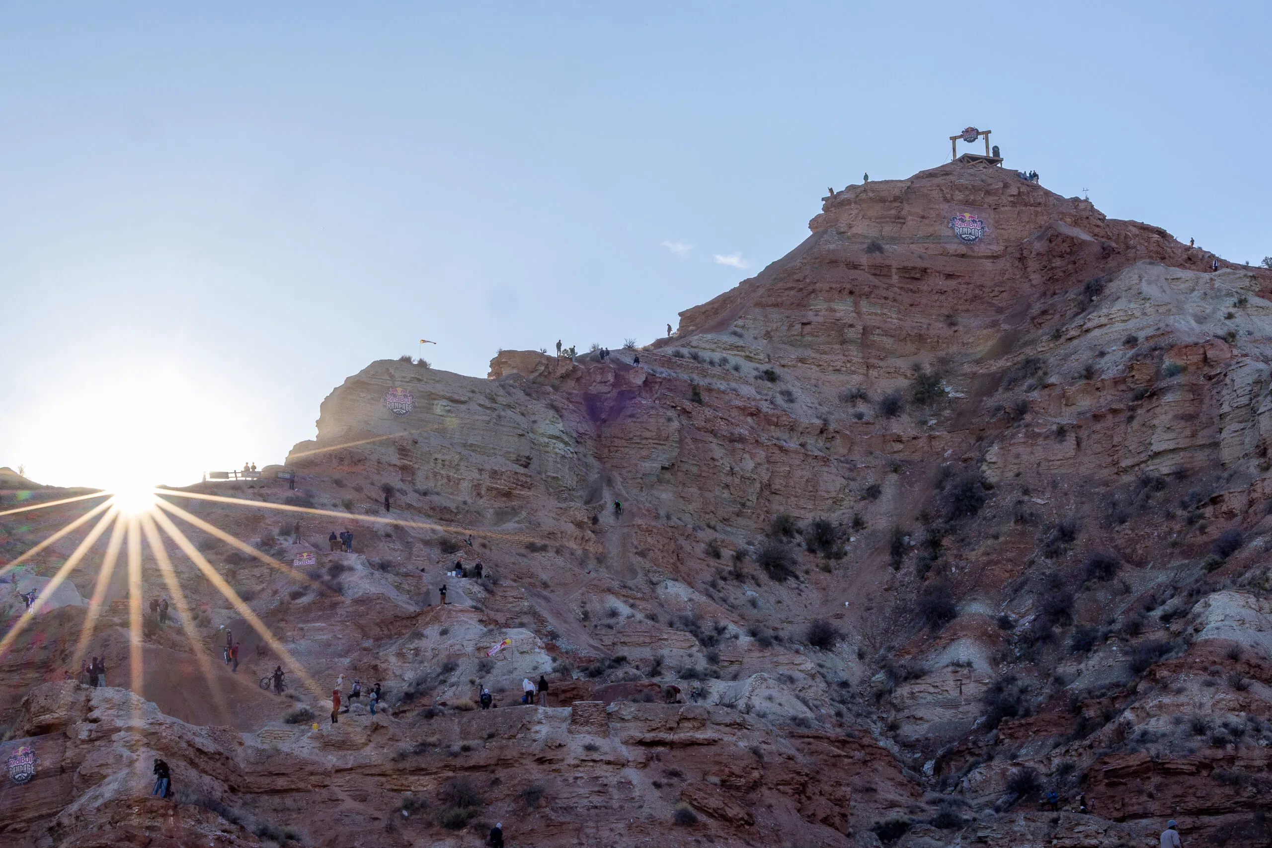 A professional action shot of a mountain biker mid-air during the Red Bull Rampage, showcasing the extreme height and desert landscape of Virgin, Utah.