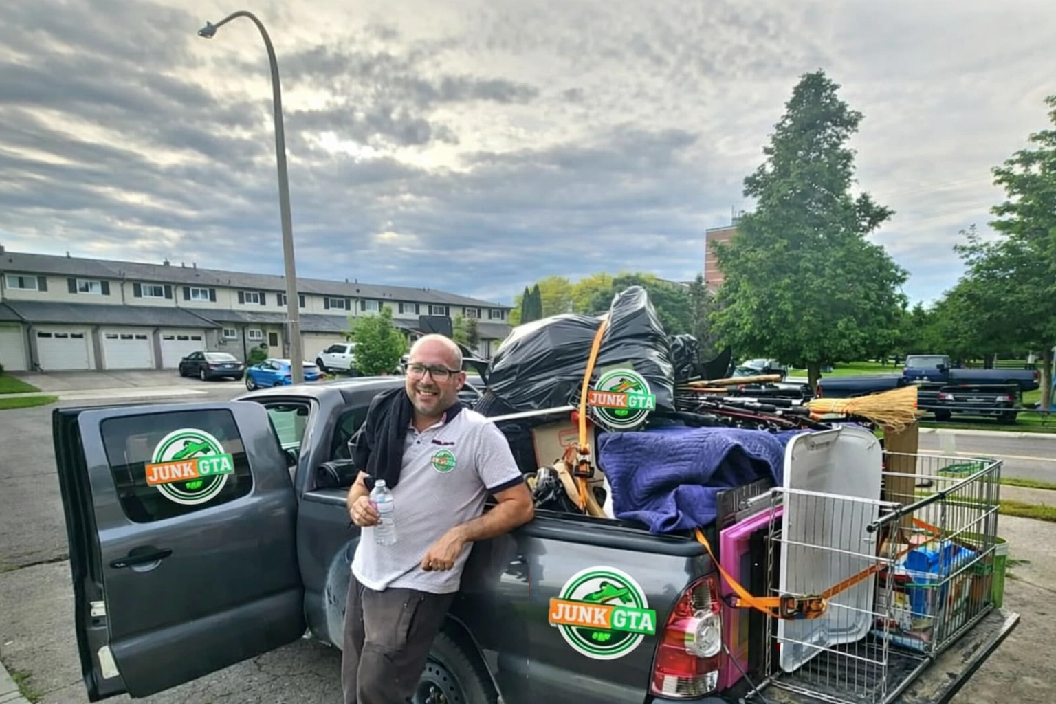 Roman, owner of Junk GTA, standing by his 2014 Toyota Tacoma loaded with junk for removal in a residential neighborhood.