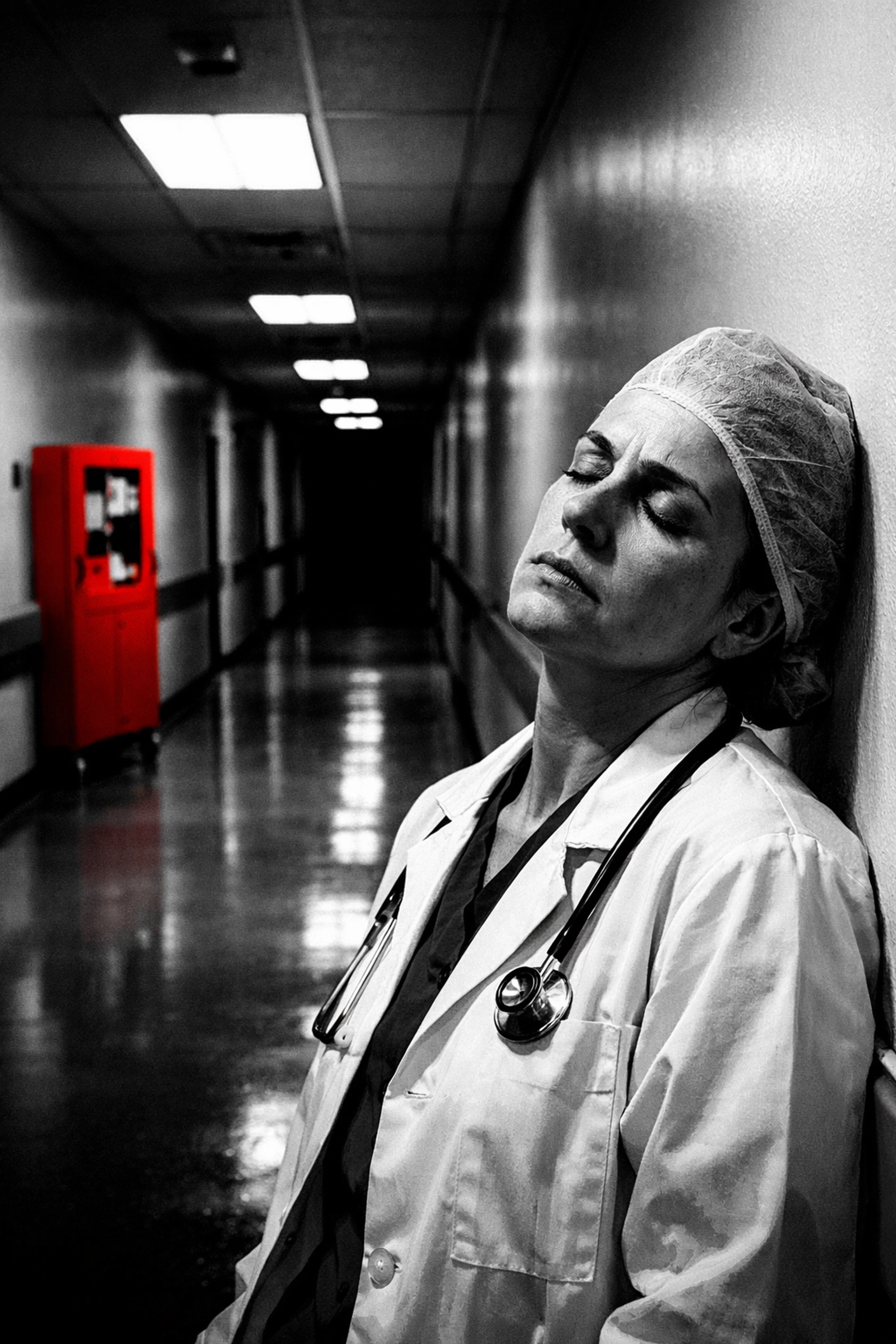 An exhausted healthcare worker rests against a hospital wall, highlighting the burnout in the medical staffing crisis.