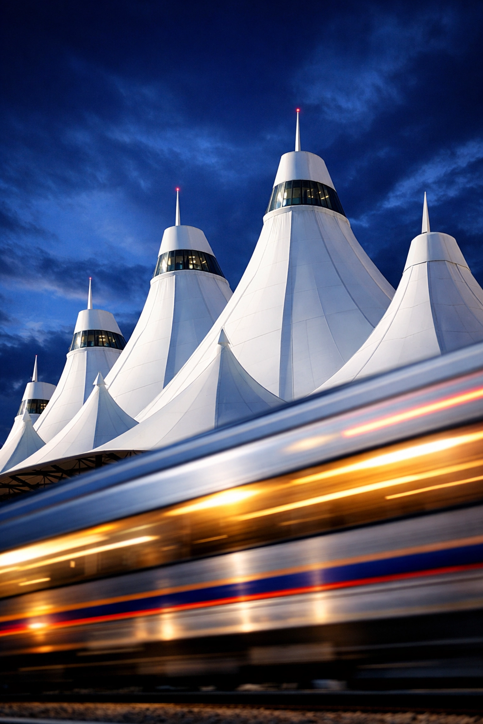 The iconic white peaked roof of Denver International Airport and A-Line train at twilight.