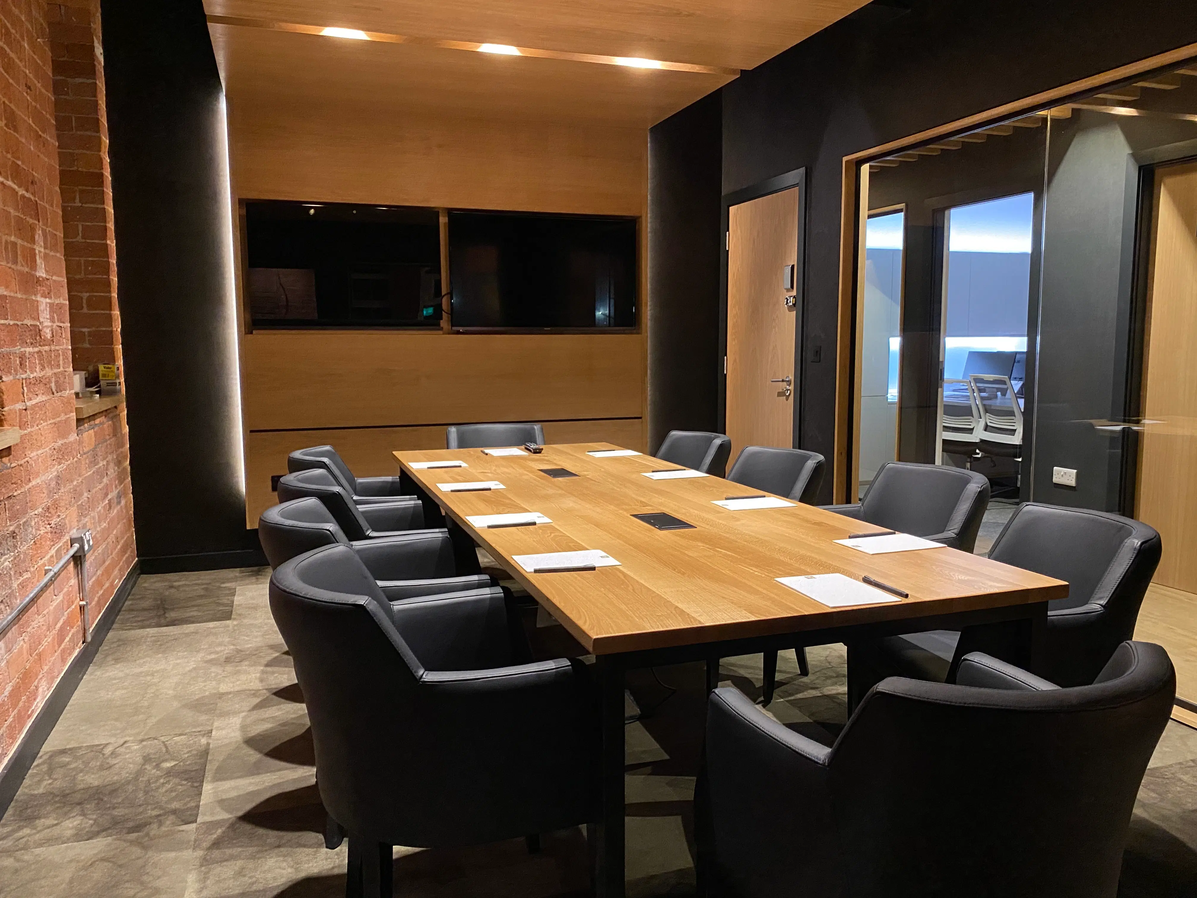 Contemporary private meeting room featuring a large wooden table, eight leather chairs, wall-mounted screens, and modern lighting.