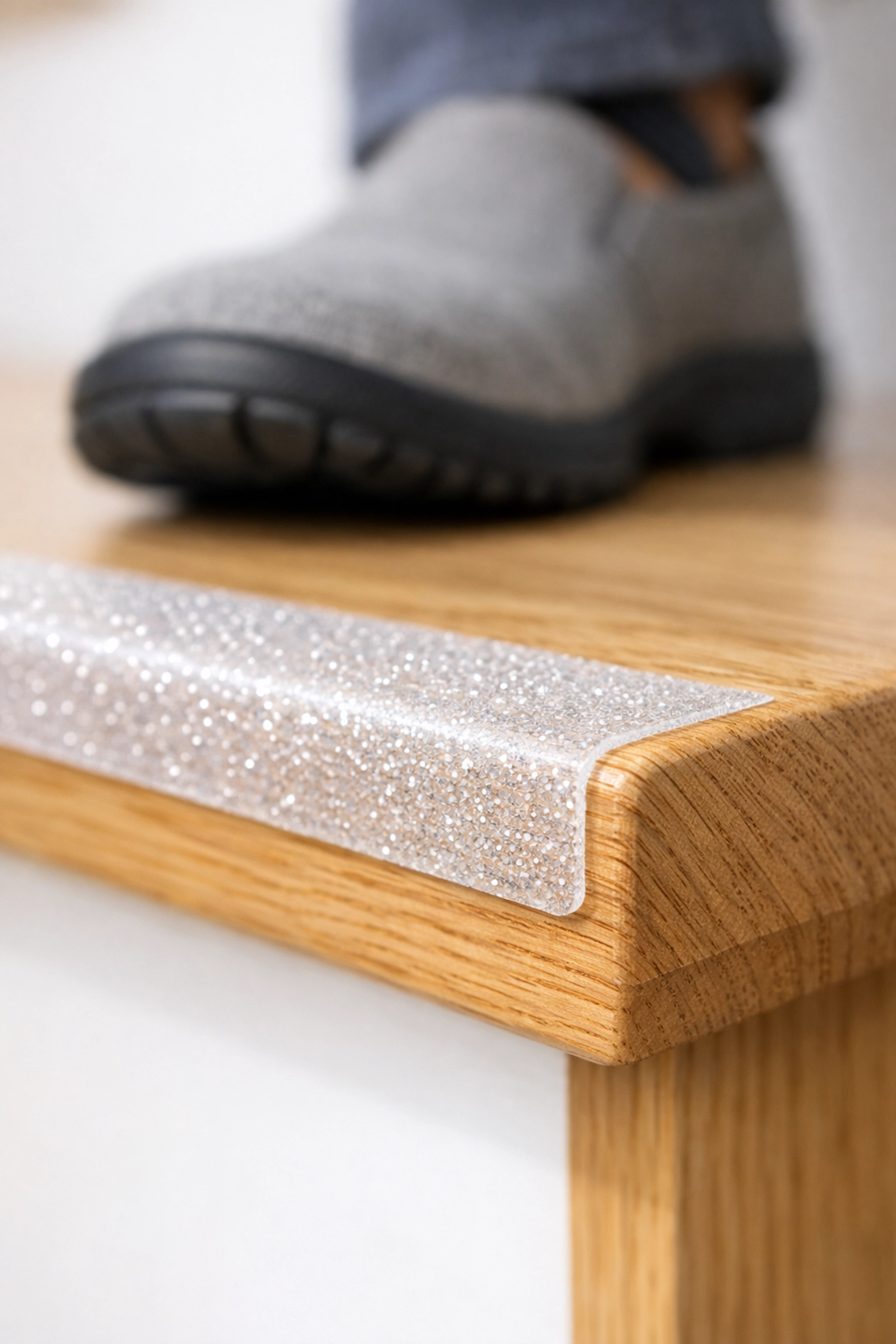 Close-up of a high-traction anti-slip strip on a wooden stair tread with a non-skid shoe nearby.