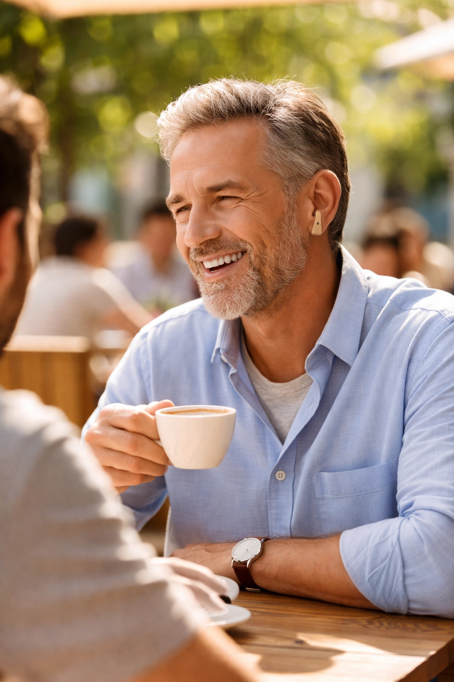 Middle-aged man enjoying conversation at a café while wearing a discreet, modern hearing aid