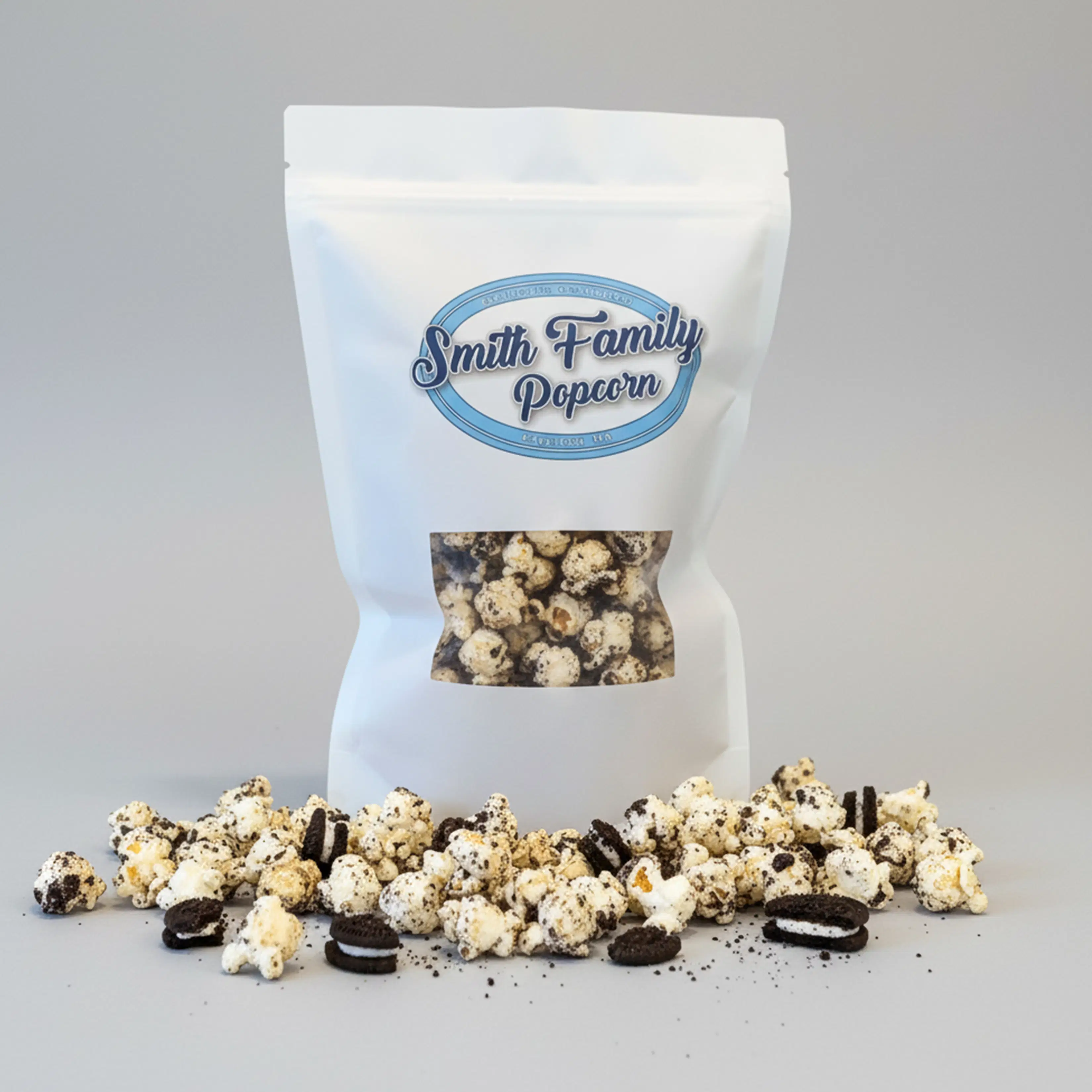 A white, resealable Smith Family Popcorn bag sits behind a scattered pile of gourmet popcorn coated in crushed chocolate sandwich cookies.