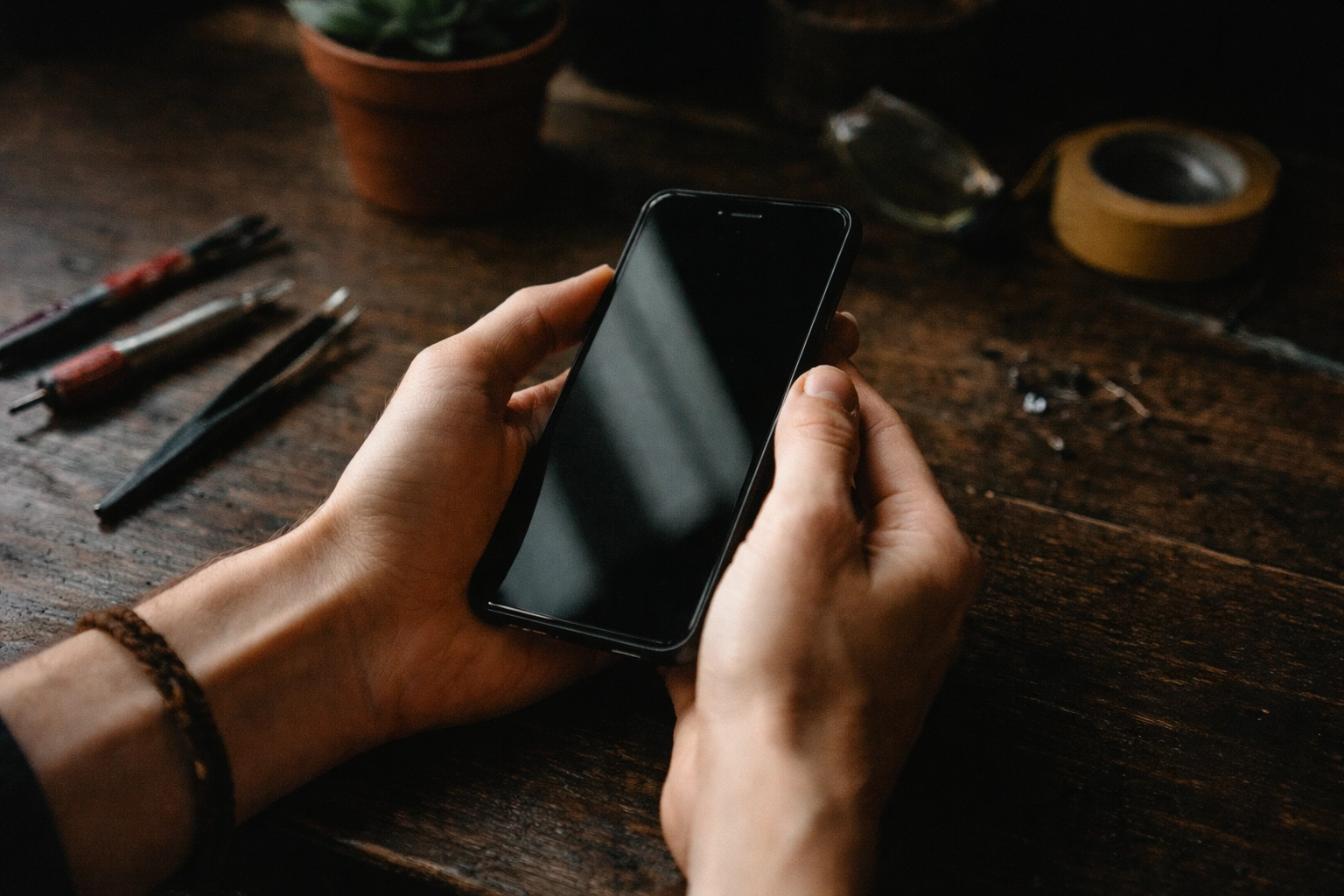 Macro close-up of hands holding a repaired iPhone with moody film grain and deep shadows, highlighting repair-not-replace.