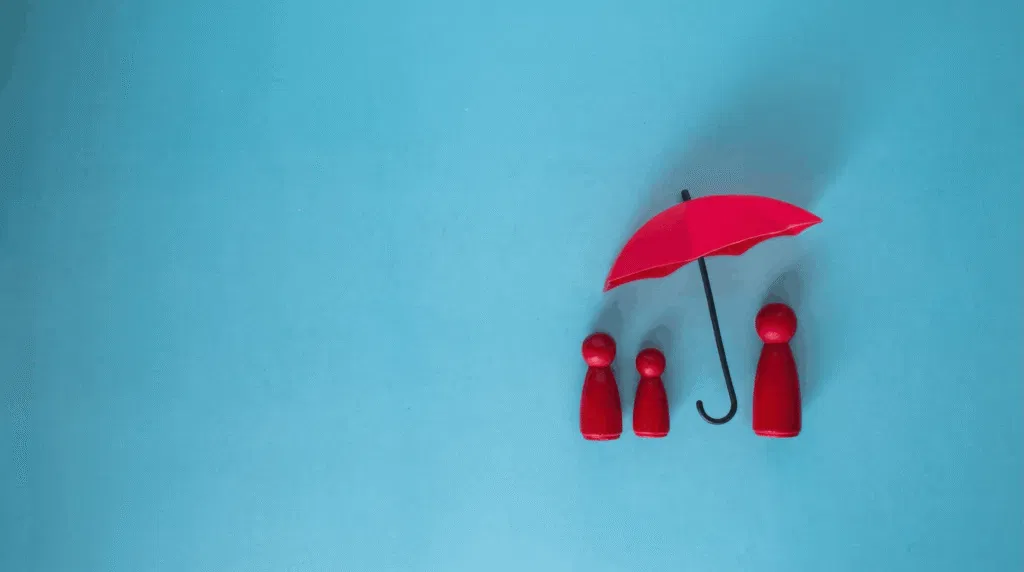 Three wooden figures symbolizing a family protected under an umbrella