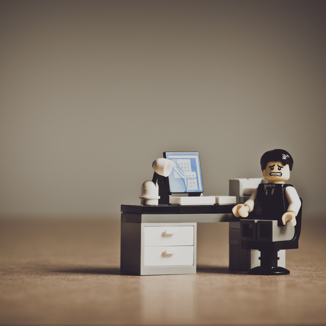 A worried office worker LEGO figure sits at a cluttered desk, representing the frustration and overwhelm before implementing Myriad’s solutions.