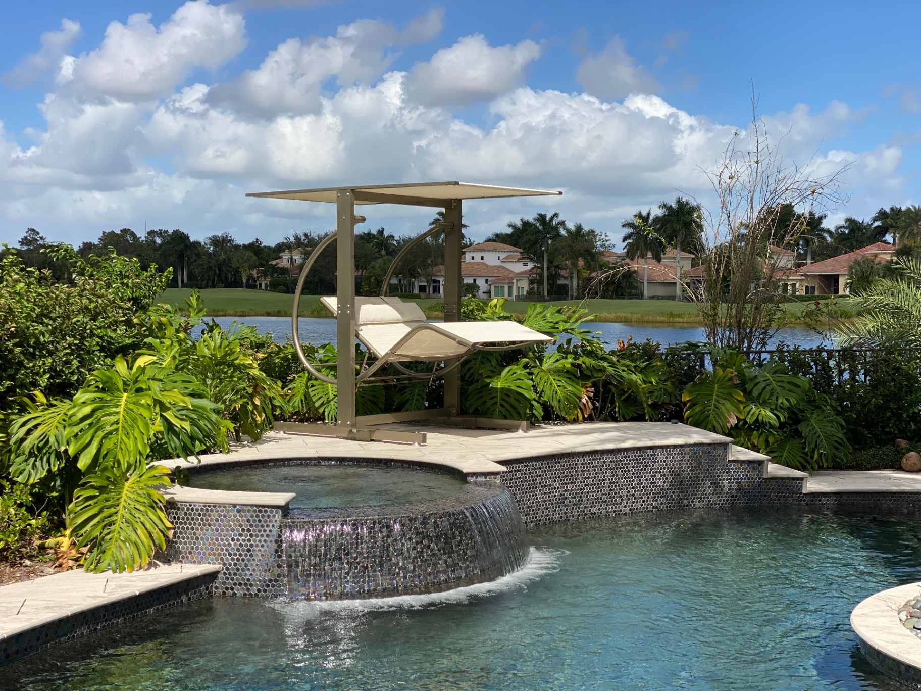 Zero Gravity Swing Double Lounge by David Frank Furniture positioned above a raised spa with a waterfall edge, overlooking a pool and lakeside view.