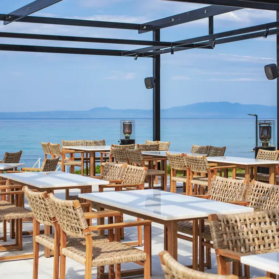 Modern outdoor restaurant terrace featuring durable woven rattan chairs and sleek white tables under a black metal pergola