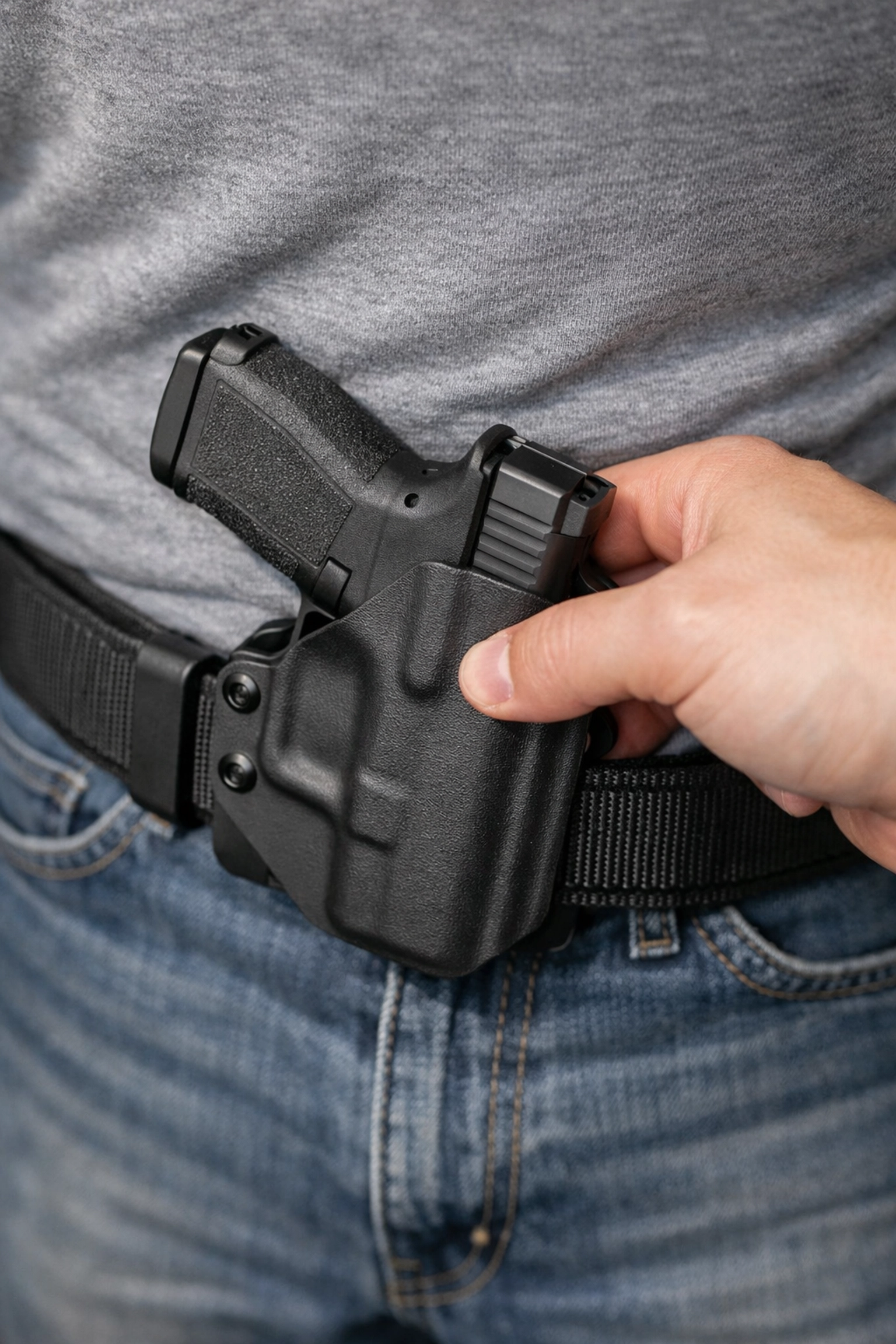 A person looking down to safely re-holster a handgun into a black Kydex appendix carry holster.