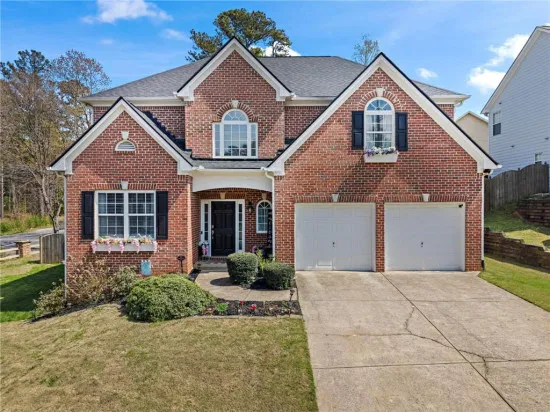 A classic two-story traditional brick home in a quiet Acworth cul-de-sac, surrounded by lush green trees and professional landscaping, framed with a colorful hand-drawn border.