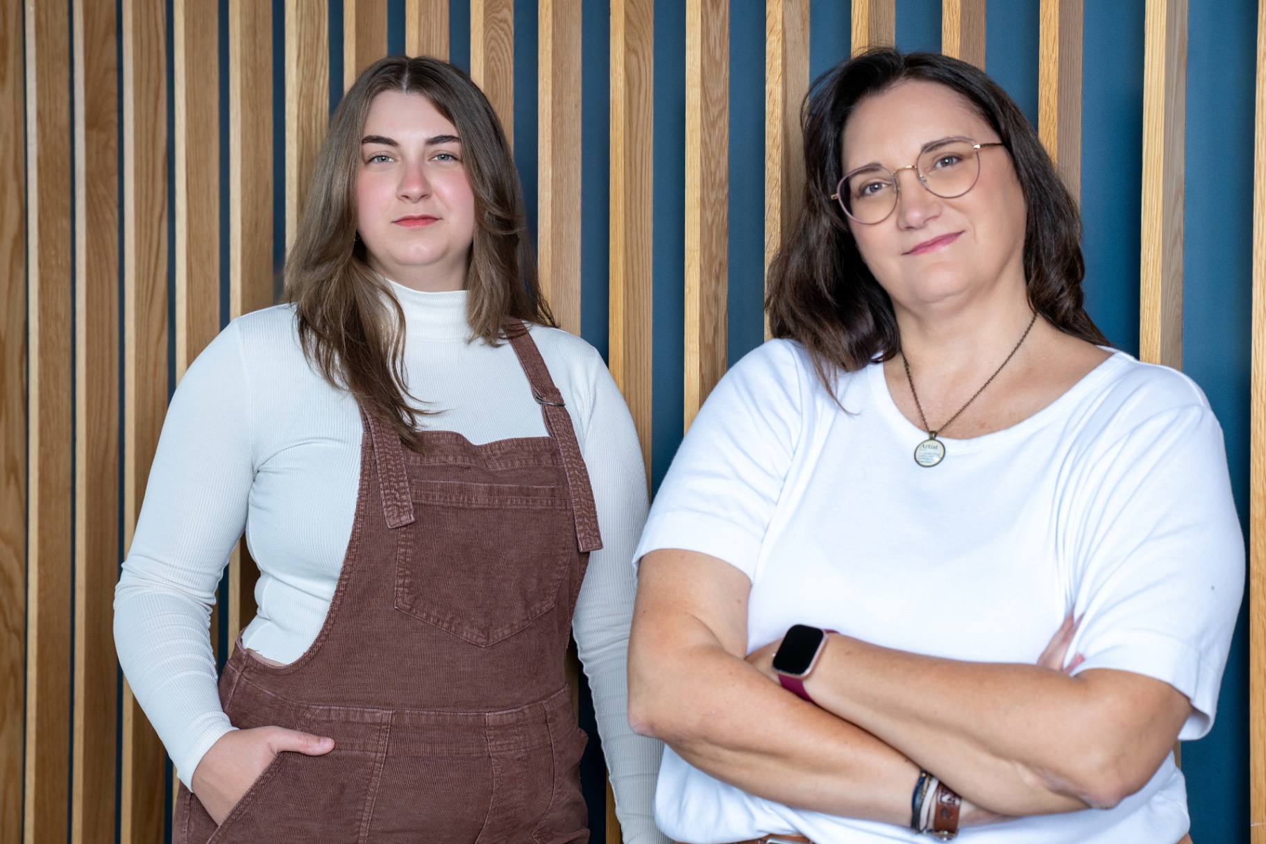 Two women standing confidently in front of a modern wood-panel wall