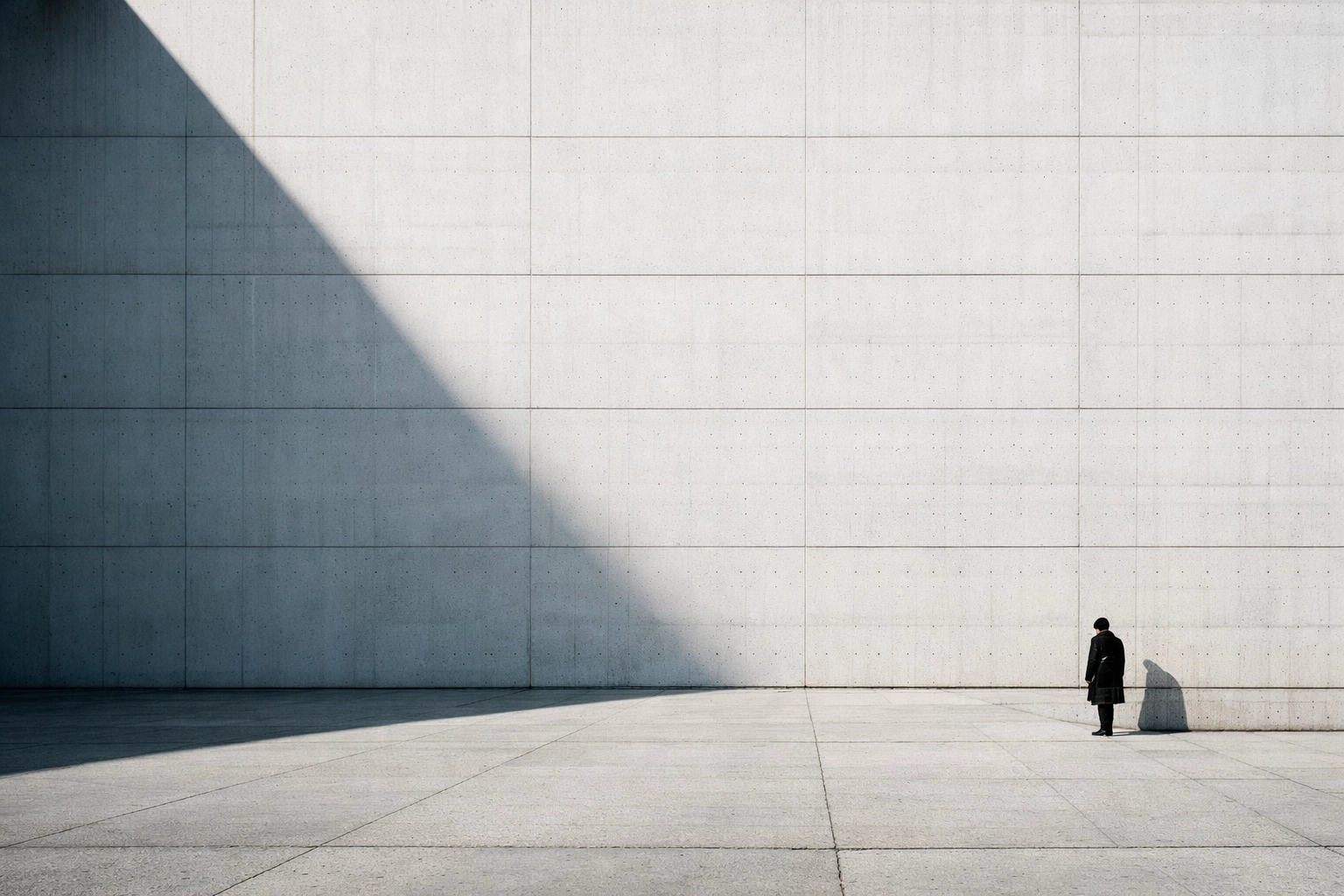 Person in a minimalist coat standing in a vast white plaza using negative space in street photography.